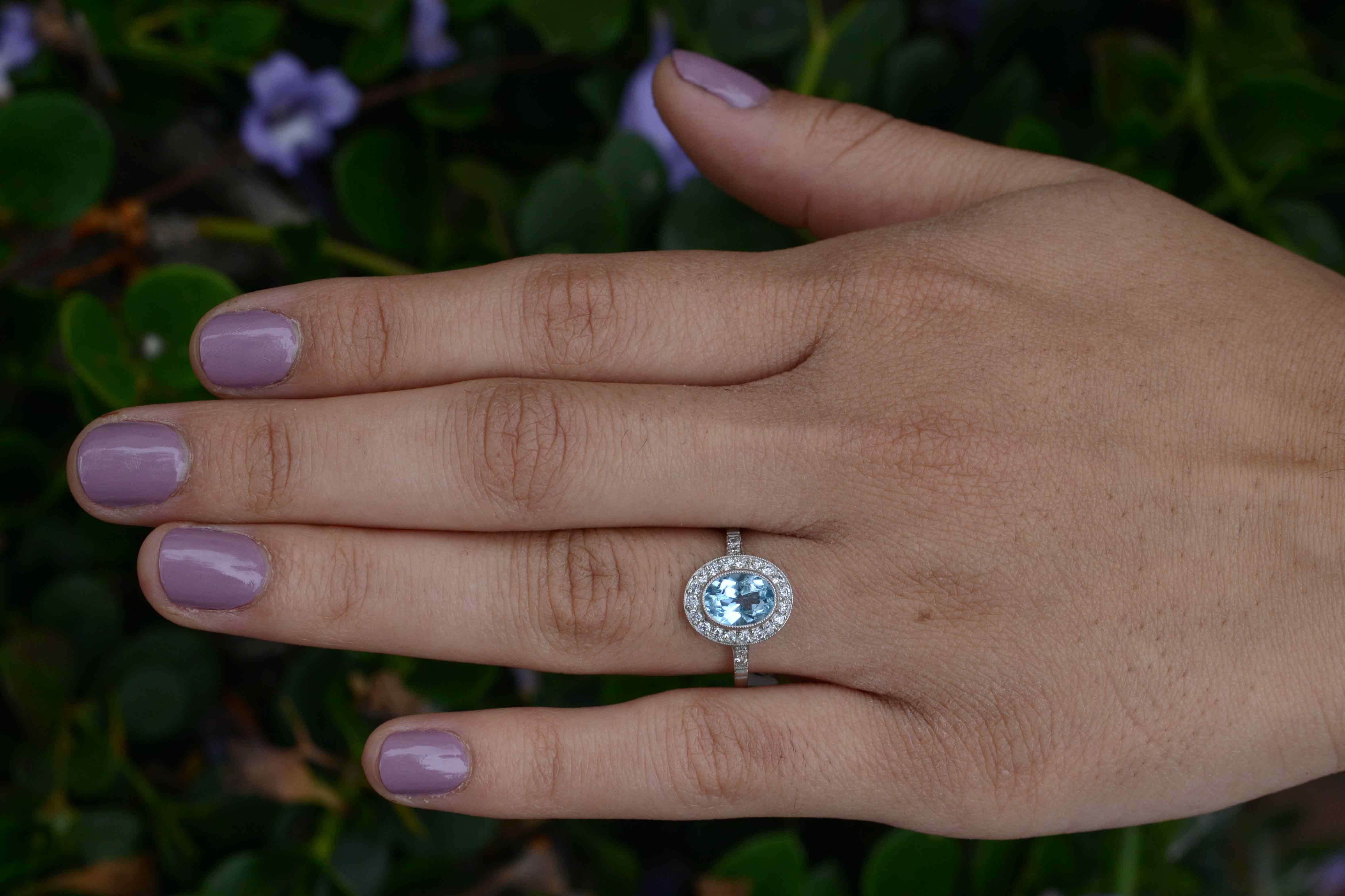 Floating in a pool of diamonds is a vivid, aqua-blue topaz engagement ring adorned with a dainty milgrain bezel. We love the oval diamond halo exhibiting a strong Art Deco geometry (and how it makes the gemstone pop). supported by a most interesting