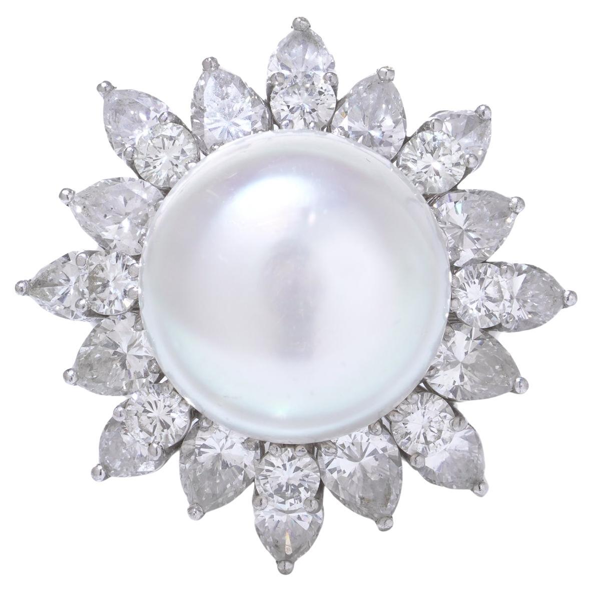 Anello vintage in platino a grappolo con una grande perla naturale rotonda incastonata in una corona di diamanti naturali. La perla presenta un corpo di colore bianco tenue con sfumature rosa, che le conferiscono una presenza raffinata ed elegante.