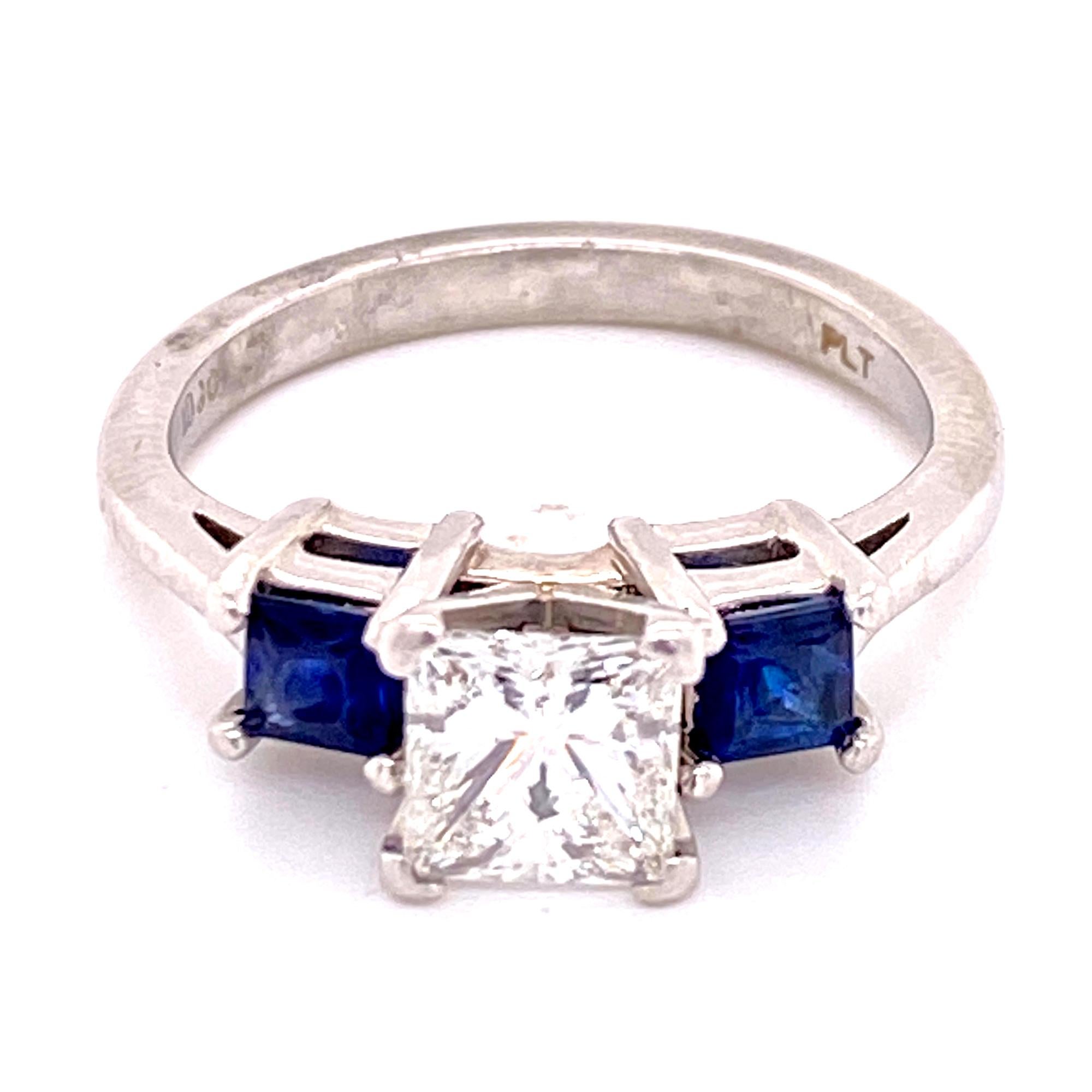 Beautiful three stone diamond and sapphire ring is handcrafted in platinum. The 1.02 princess cut diamond is GIA certified and graded G color and VS2 clarity. The center diamond is set between two beautiful blue princess cut natural sapphires