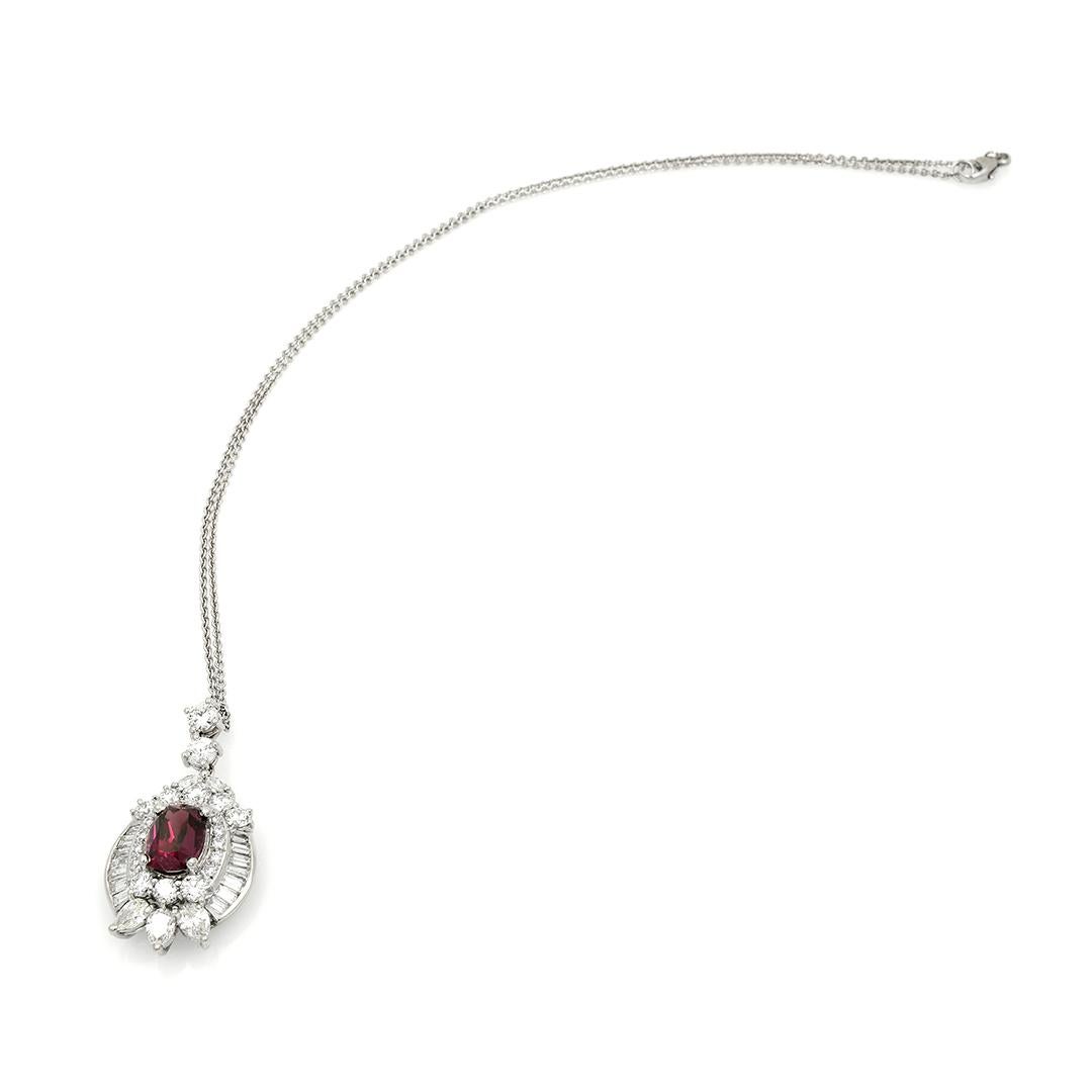 This platinum pendant features an approximately 3.24 carat red oval Rhodolite surrounded by 23 round brilliant cut diamonds, 14 baguette diamonds, 2 marquise diamonds, and 3 pear-shaped diamonds weighing an approximate combined 4.00 carats. There is