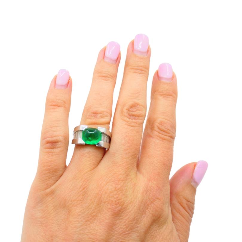 An architectural platinum ring, featuring emerald and diamond.
The ring has a strong, structured design with the band features a stepped setting that secures a
cabochon emerald. Flanking the emerald, channel set baguette diamonds run along the sides