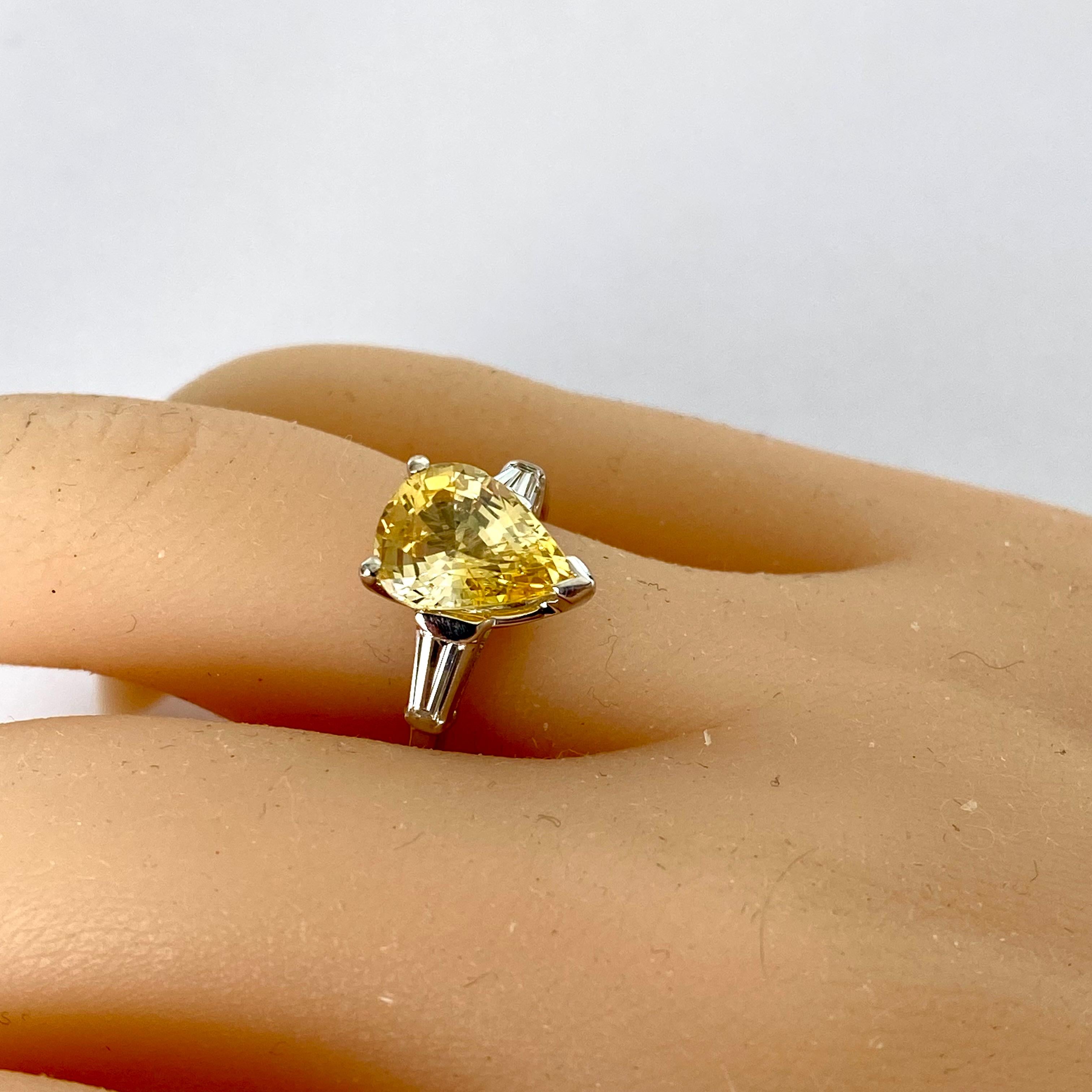 Dieser exquisite Verlobungsring aus Platin mit einem atemberaubenden gelben Ceylon-Saphir in Birnenform und zwei schillernden Baguette-Diamanten verleiht Ihrer Liebesgeschichte eine ganz besondere Note. Dieser in Perfektion gefertigte Ring