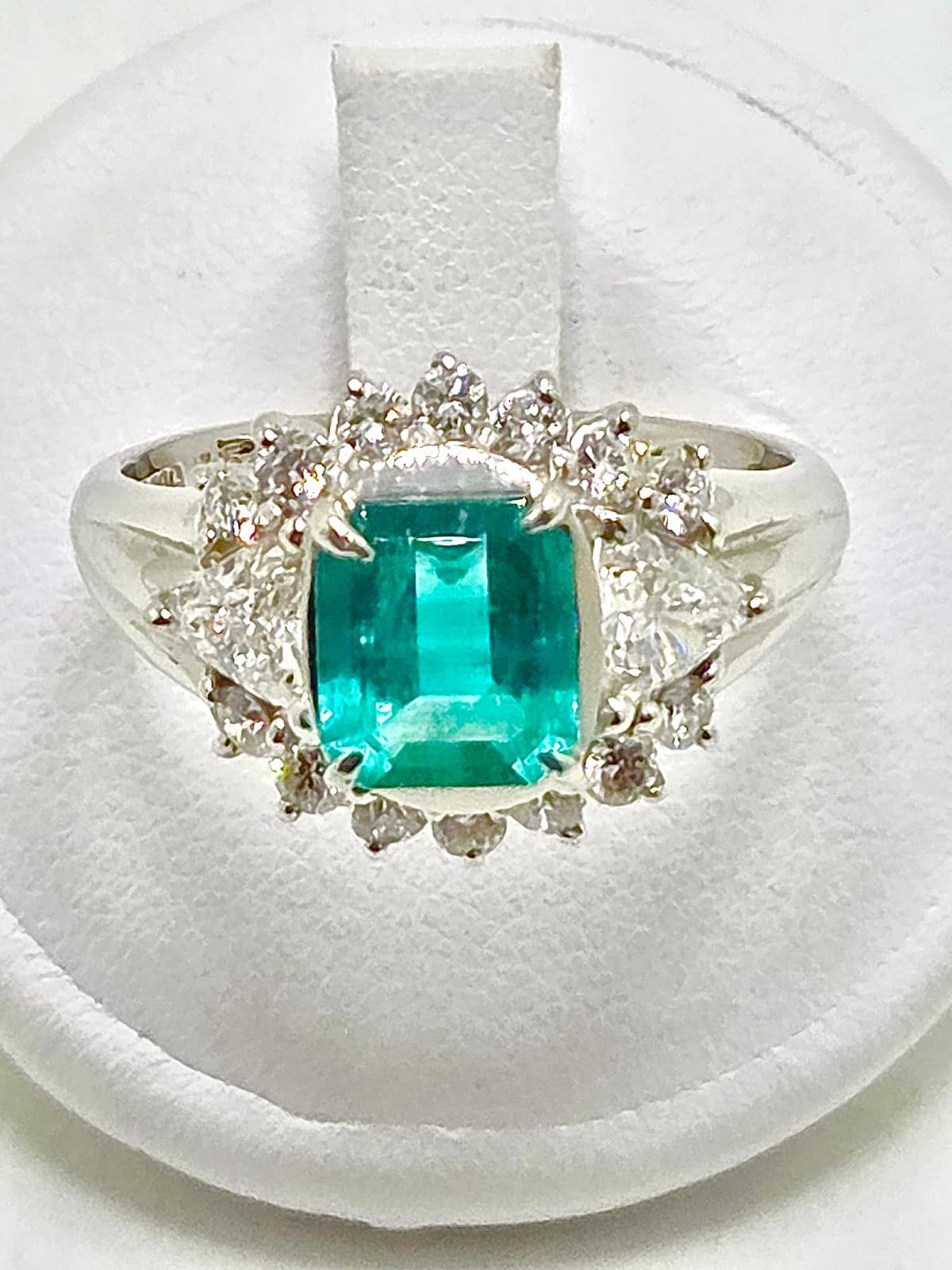 A spectacular platinum ring centered with a vibrant natural emerald weighing 1.54 carats, admired for its rich green color and natural beauty. The emerald is elegantly complemented by a pear-cut diamond of 0.60 ct and additional brilliant-cut