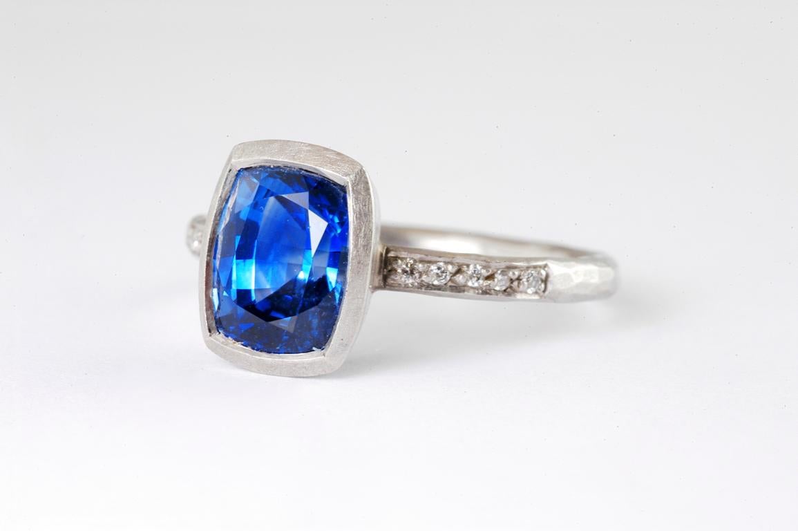 2mm hammered platinum ring with cushion shaped sapphire 3.05cts and channel set diamonds 0.10cts total approx handmade in Notting Hill London by renowned British jewellery designer Malcolm Betts.
A comfortable 2mm hammered platinum set with blue,