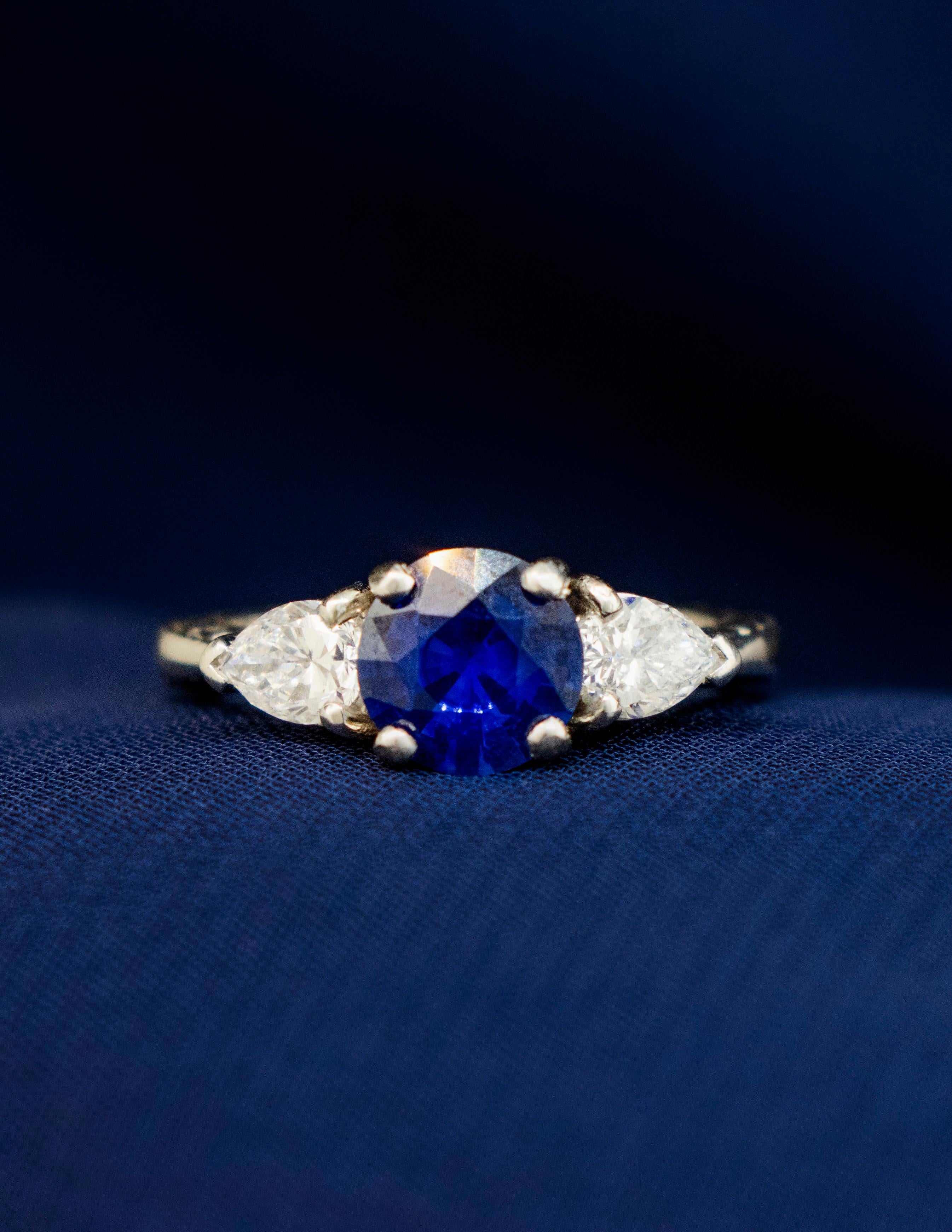 A Ladies Platinum Ring mounted with a Round Cut Kashmir Blue Sapphire with Pear Shape Diamonds. The center stone is a 1.31 carat Sapphire exhibiting exceptional brilliance, deep, true blue color and intense scintillation. The pear brilliant diamonds