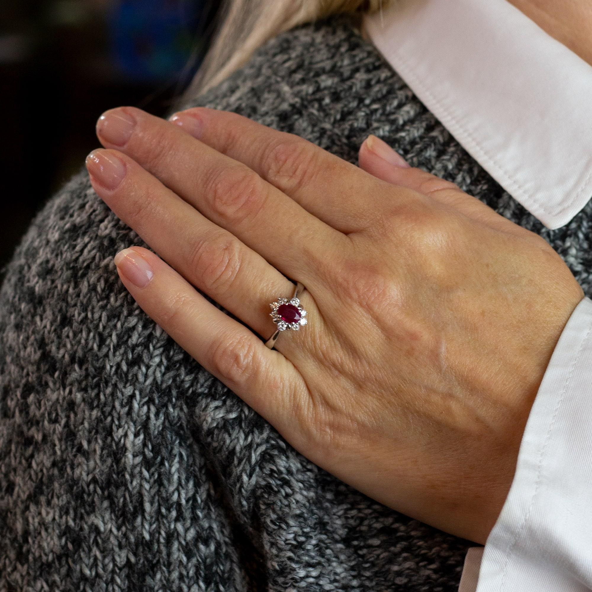 A lovely classic ruby and diamond ring set in platinum. The 9 stone ring features a central oval cut ruby classified as 'moderately bright, mid pinkish red and moderately included' weighing 0.76 carat. This beautifully coloured stone is halo set