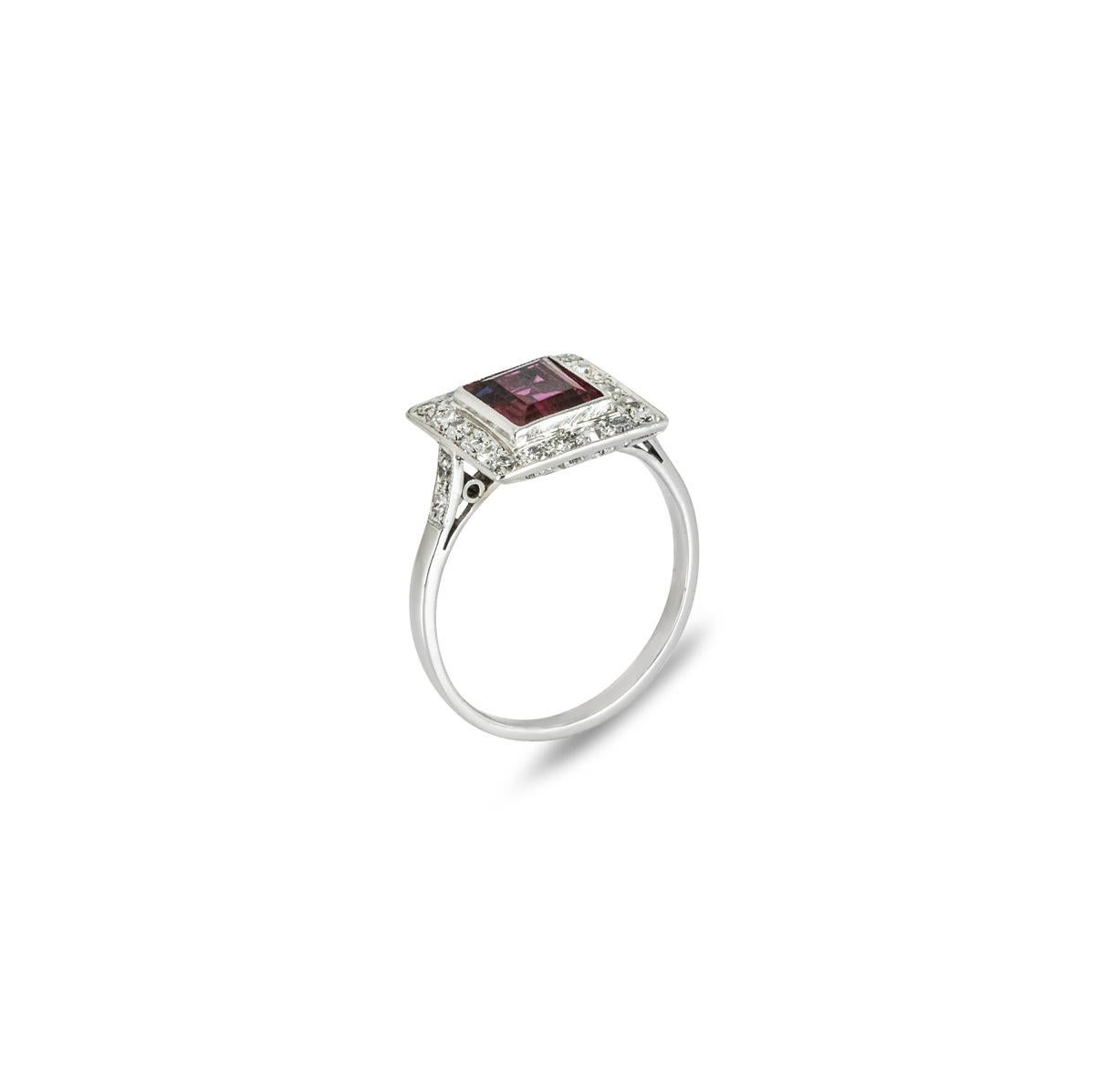 A timeless platinum ruby and diamond dress ring. Set to the centre in a bezel mount is a rectangular cut ruby weighing approximately 1.30ct and displaying a medium-dark purplish-red hue. Accentuating the ruby are 24 single cut diamonds set around