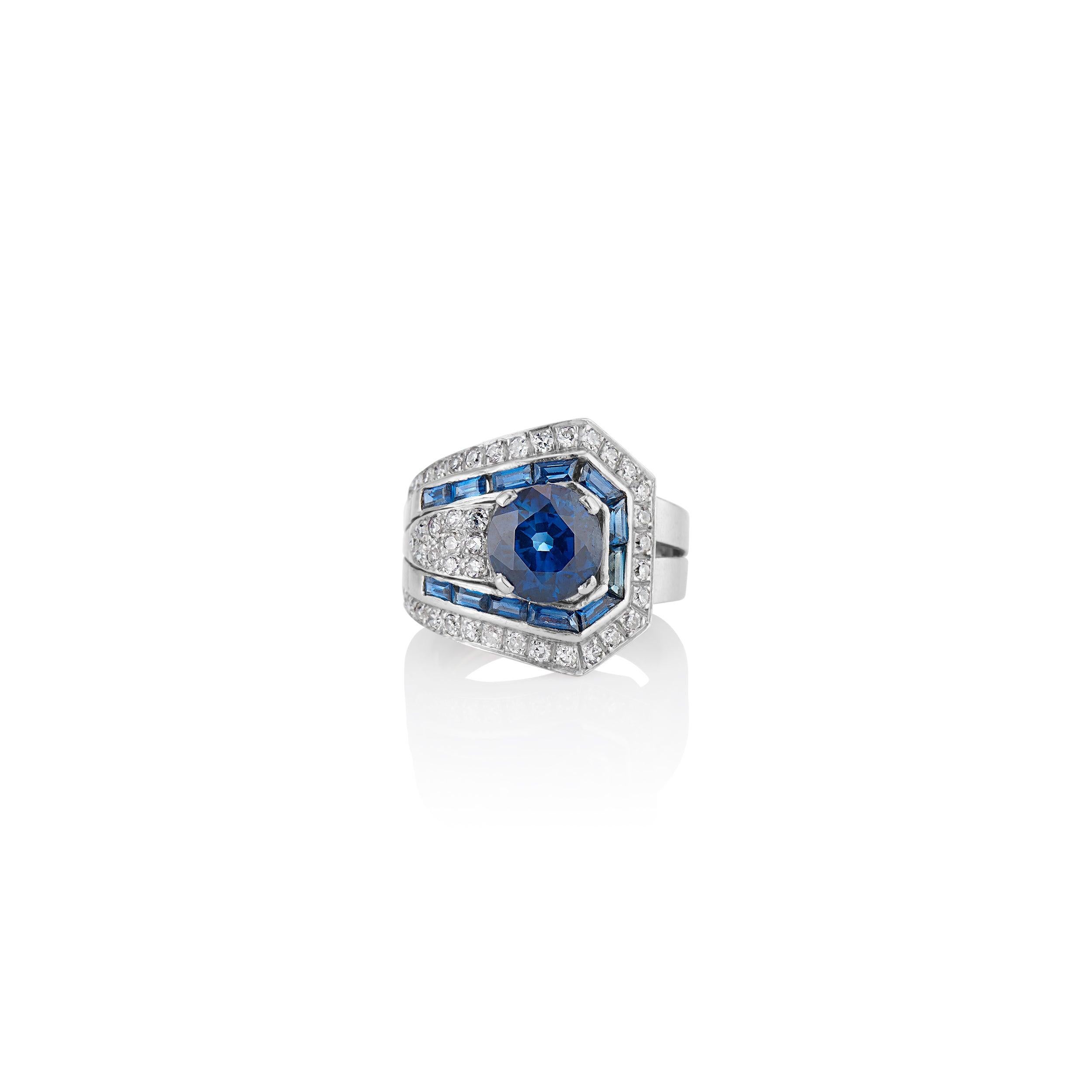 Masterfully hand crafted in platinum, this stylized buckle ring boasts a 3.82 carat royal blue sapphire embraced by a triangular section of pave-set diamonds, bordered by a single row of sleek calibre-cut sapphires and sparkling single-cut diamonds.