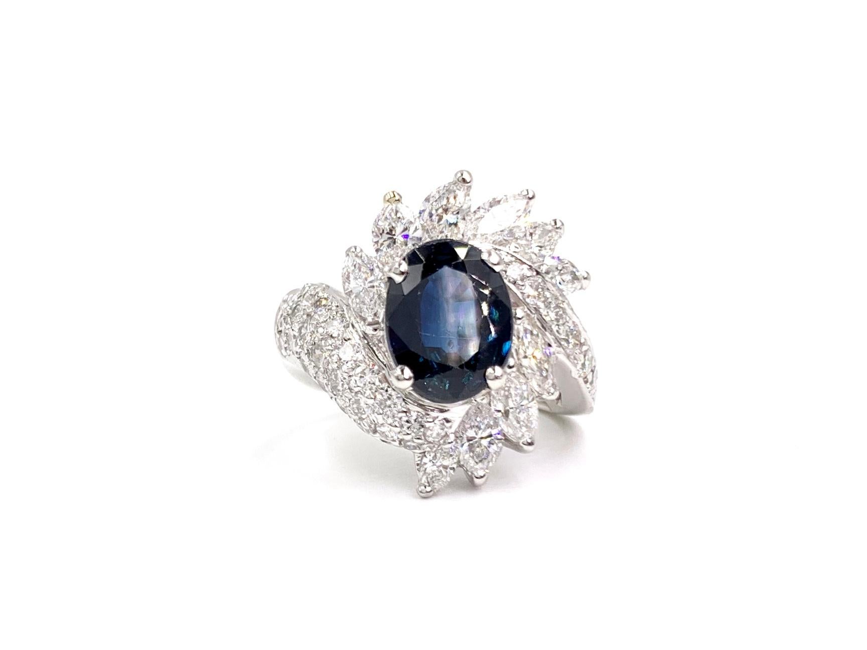 A 2.95 carat oval dark blue sapphire is beautifully surrounded by marquise cut and round brilliant white diamonds in this platinum cocktail ring. 10 Marquise cut and 31 round brilliant diamonds have a total weight of 2.32 carats with quality of