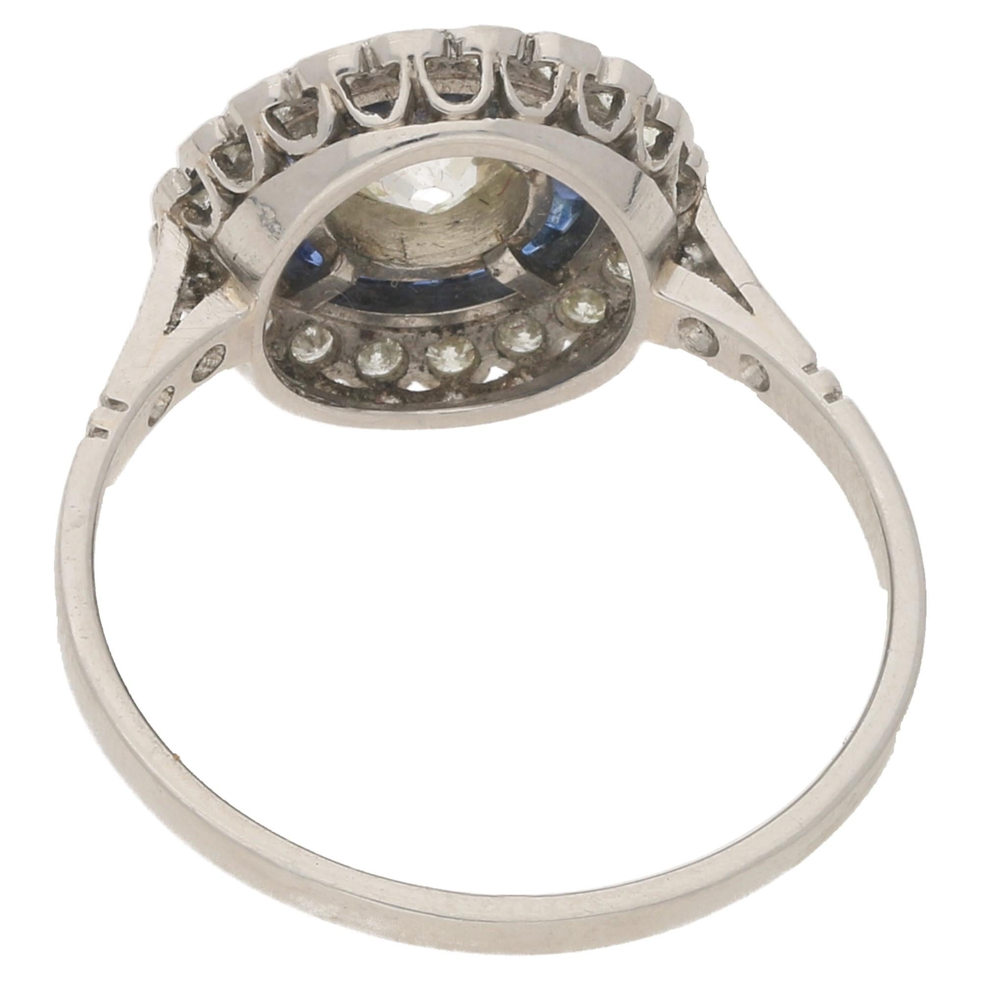 An Art Deco style diamond and sapphire coronet cluster target ring in platinum, featuring an Old Mine-cut diamond at the centre with approximately 0.60 carats, H/I colour (assessed) and SI clarity (assessed) bezel-set to the centre within a