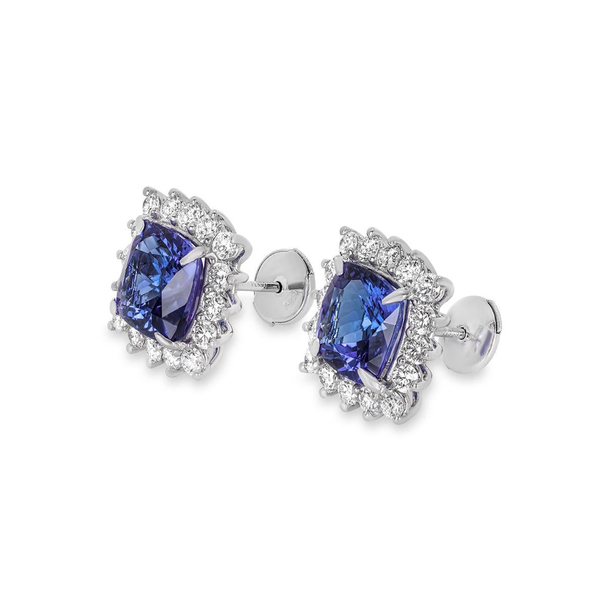 An alluring pair of platinum tanzanite and diamond stud earrings. The earrings are set to the centre with cushion cut tanzanites with an approximate total weight of 7.14ct and displaying a vivid violet-blue hue. Accentuating each tanzanite is a halo