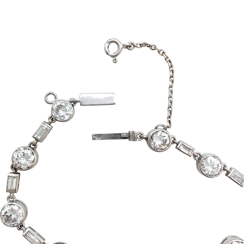 A platinum tennis bracelet set with 10 bezel set circular-cut diamonds, each link of round stone is separated by a bezel set baguette cut diamond. 
White gold clasp with a safety chain (modern).
Total weight of diamond : about 7 carats
Diamond