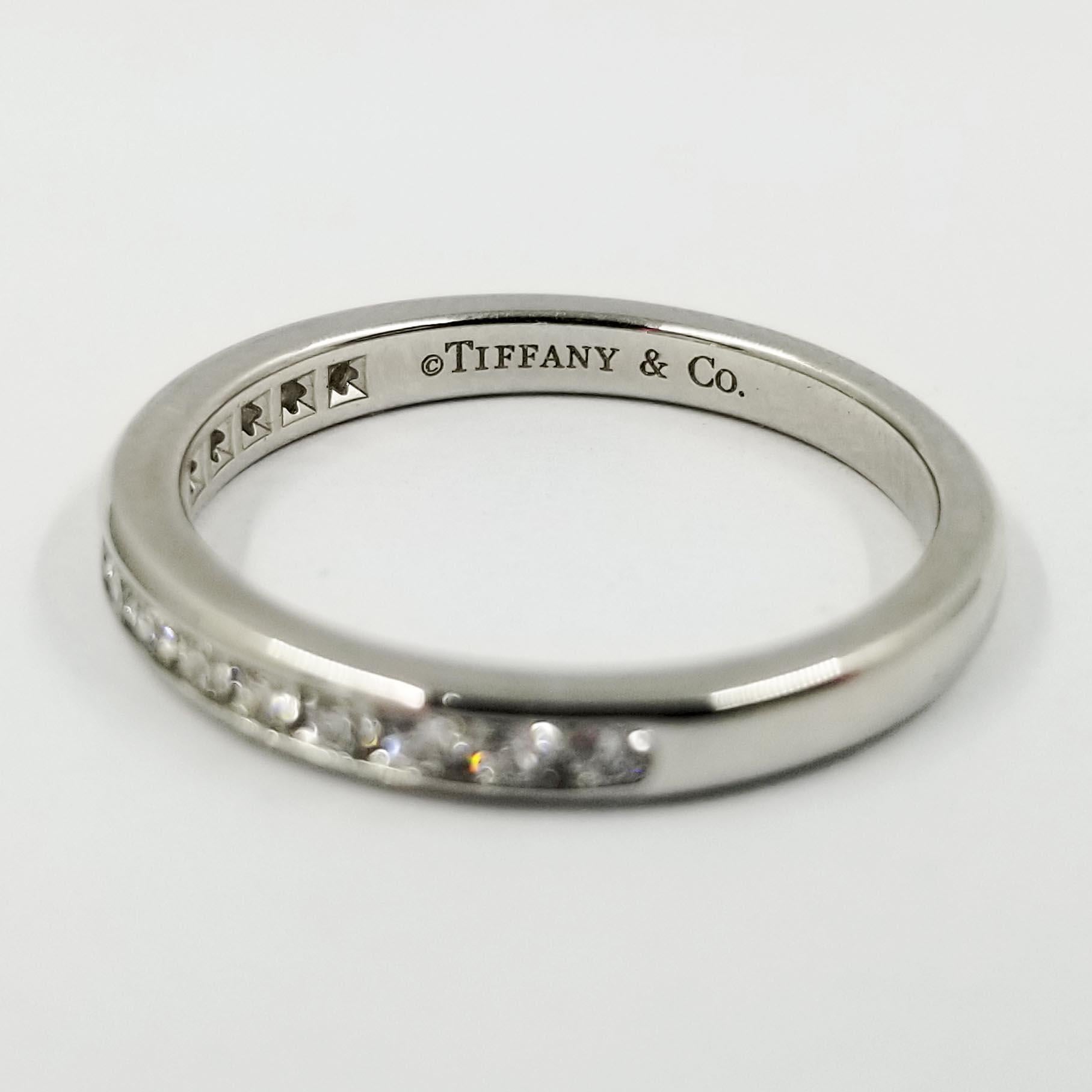 Este clásico anillo de diamantes está fabricado en platino por Tiffany & Co. Presenta 15 diamantes redondos de talla brillante engastados en canal, de color F y claridad VVS, con un peso total aproximado de 0,25 quilates. El interior lleva el sello