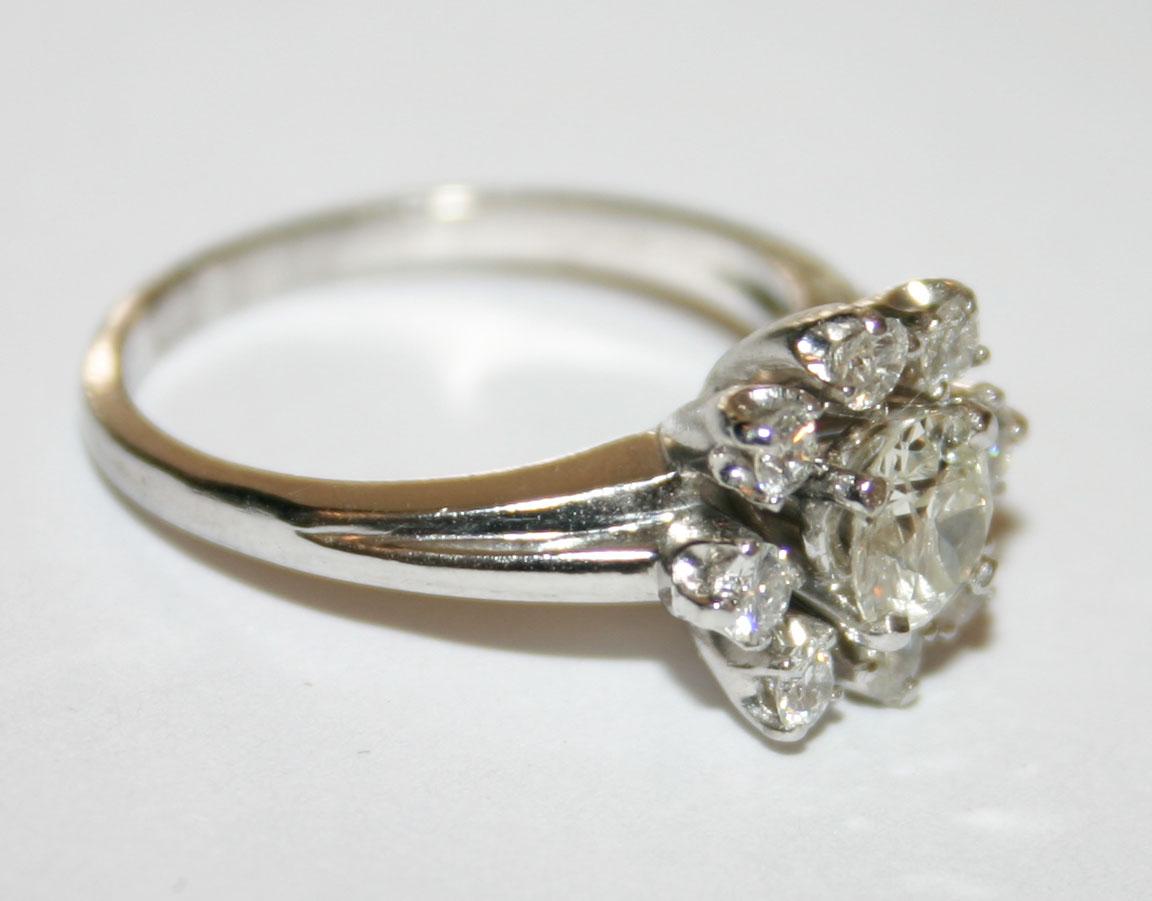 This stunning, vintage platinum cluster style ring weighs 7.40 grams.

It contains a 5.25mm diamond mounted in the center, with a carat weight of 0.55, a SI1 clarity, and a K color.

There are eight small round brilliant diamonds mounted in a prong