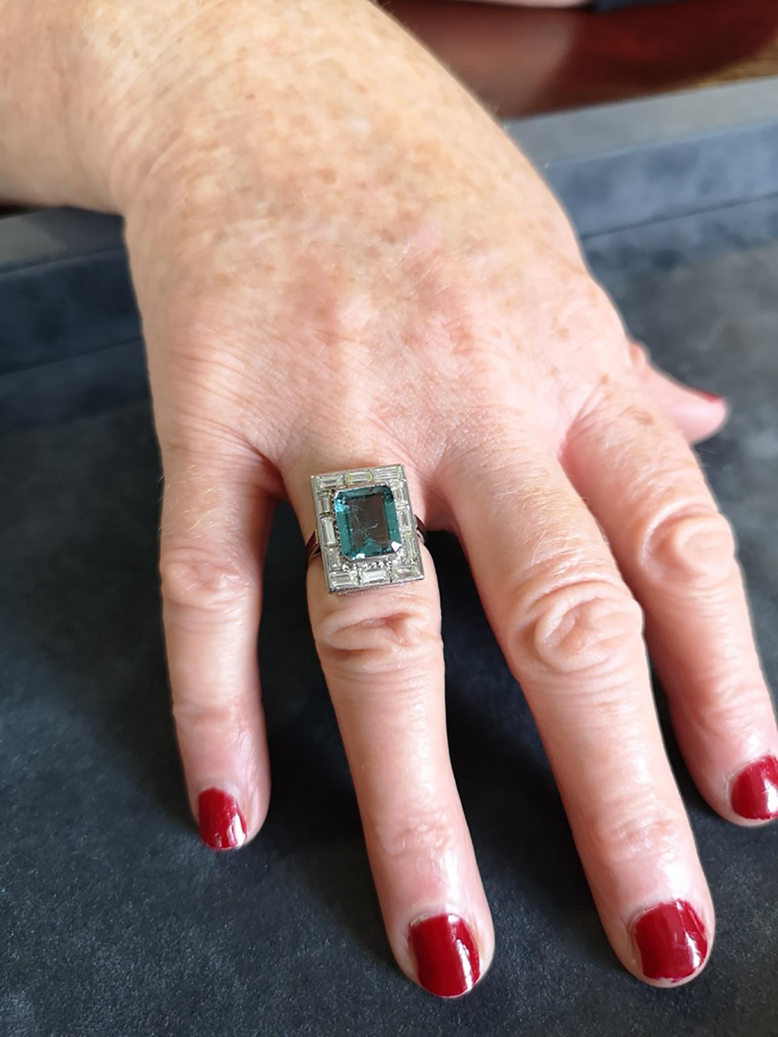 A fine quality, late 20th Century aquamarine and diamond cluster cocktail ring in platinum. The central emerald-cut aquamarine of approximately 7.00 carats and exceptional colour, mounted between two parallel platinum bars and surrounded by a border