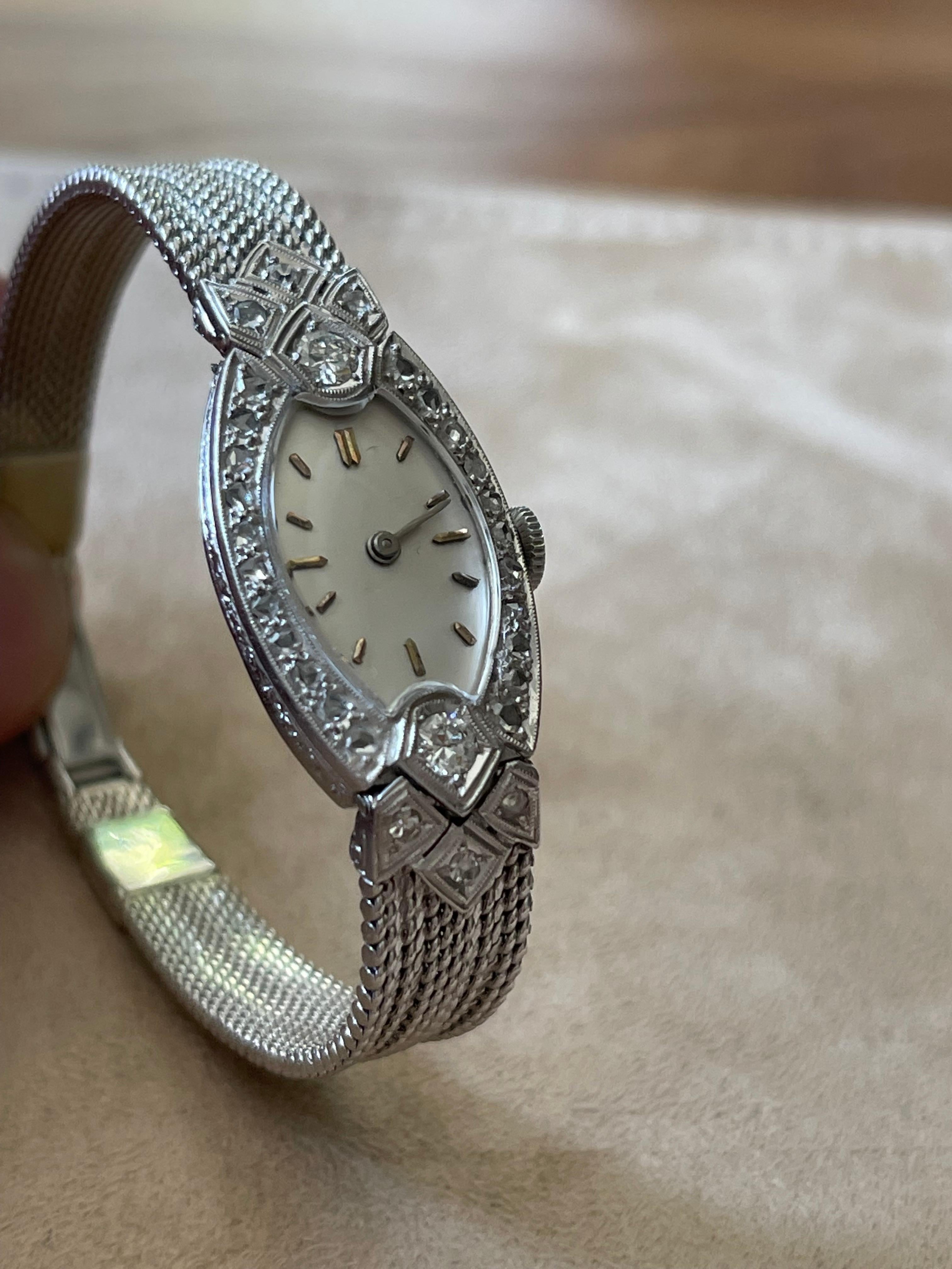 Diese atemberaubende und sehr elegante ovale Art Deco Armbanduhr aus dem Jahr 1920 besitzt ein Gehäuse aus Platin und Diamanten sowie stilisierte Ziffern auf dem Zifferblatt. Das Netzband aus Weißgold ist glatt und geschmeidig und hat eine