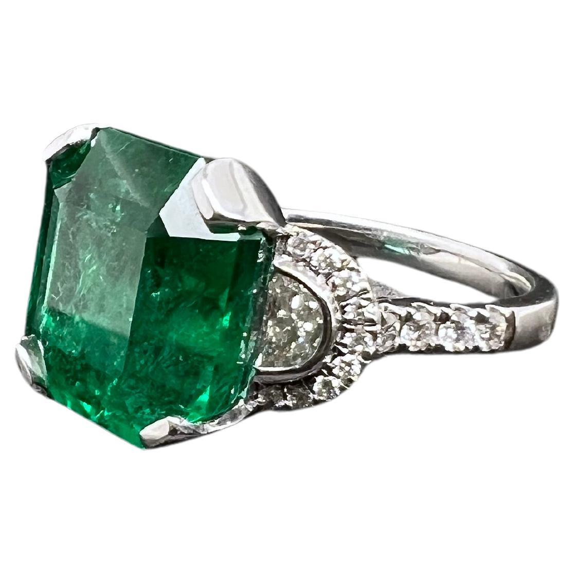 This vibrant Zambian emerald is set in a modified 3 stone style ring with 2 half moon diamonds on the sides with round brilliant diamonds finishing off the masterpiece. The lust, green emerald is the focal point and showcases amazing color in this