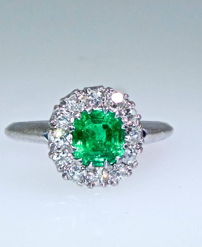 The center Colombian emerald weighs approximately .50 cts., and displays a bright clean green with no undertones.  It is surrounded by white old cut diamonds.  These 12 diamonds are each held by 12 prongs.  The weight is approximately .45 cts., very