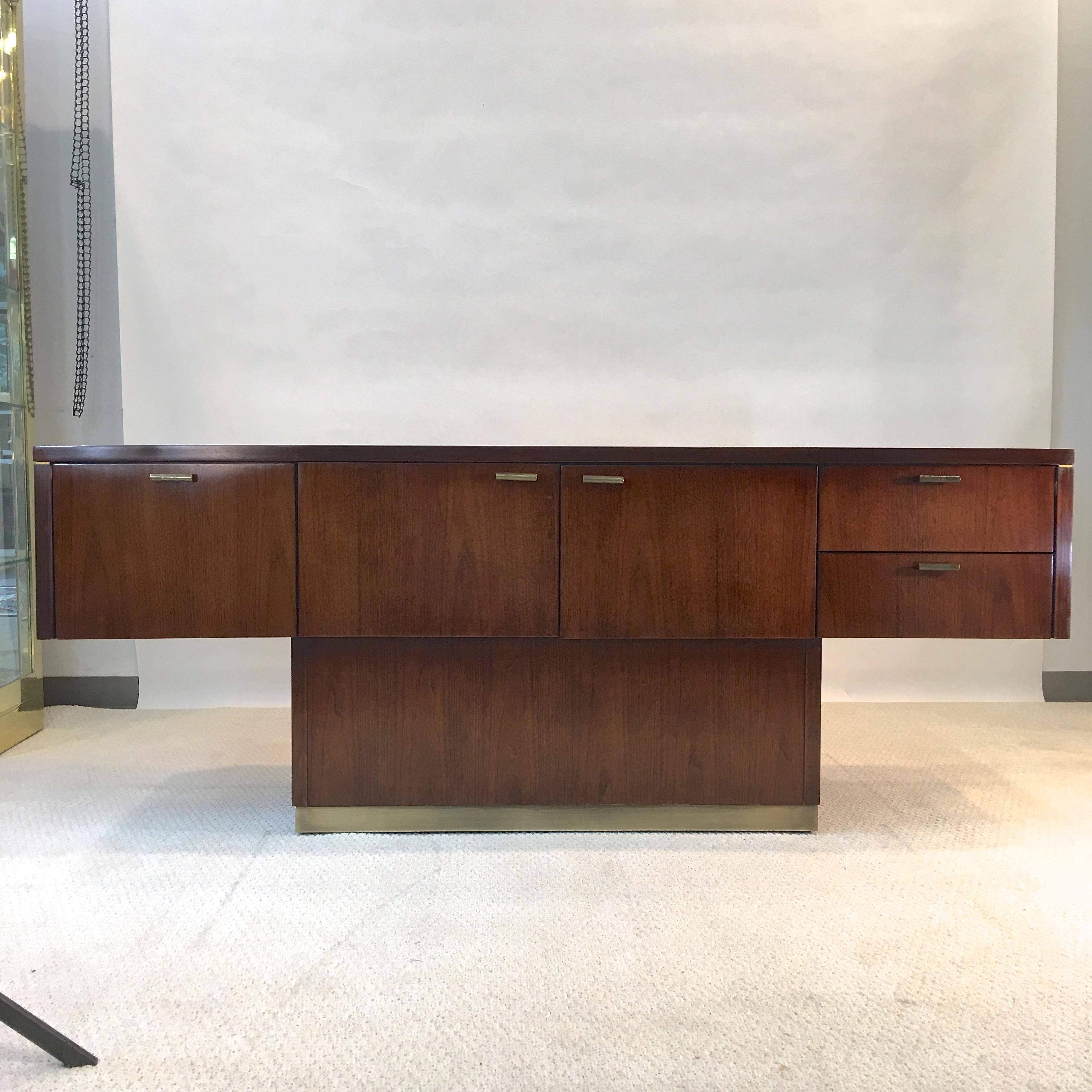 Warren Platner style 1970s architectural floating sideboard in walnut with bronze hardware and plinth base.
Finished on all sides so it can be placed anywhere in a room. 
First door is actually a deep file hanging drawer.
Middle two doors open to