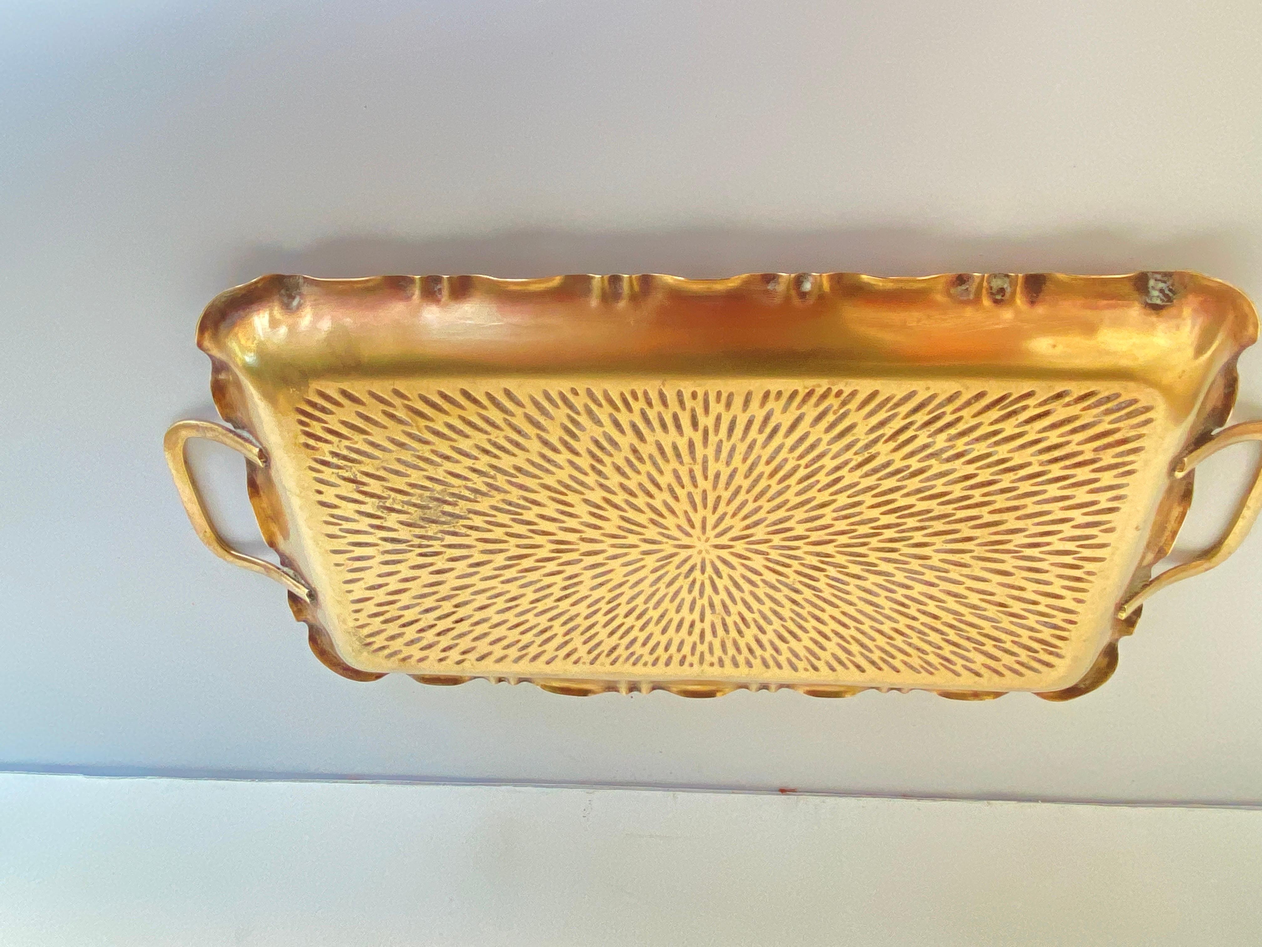 It is a tray from the Art Deco period, in brass with geometric patterns. It is equipped with two handles that allow it to be carried. It was made in France around the 1940s. It is gold in color.