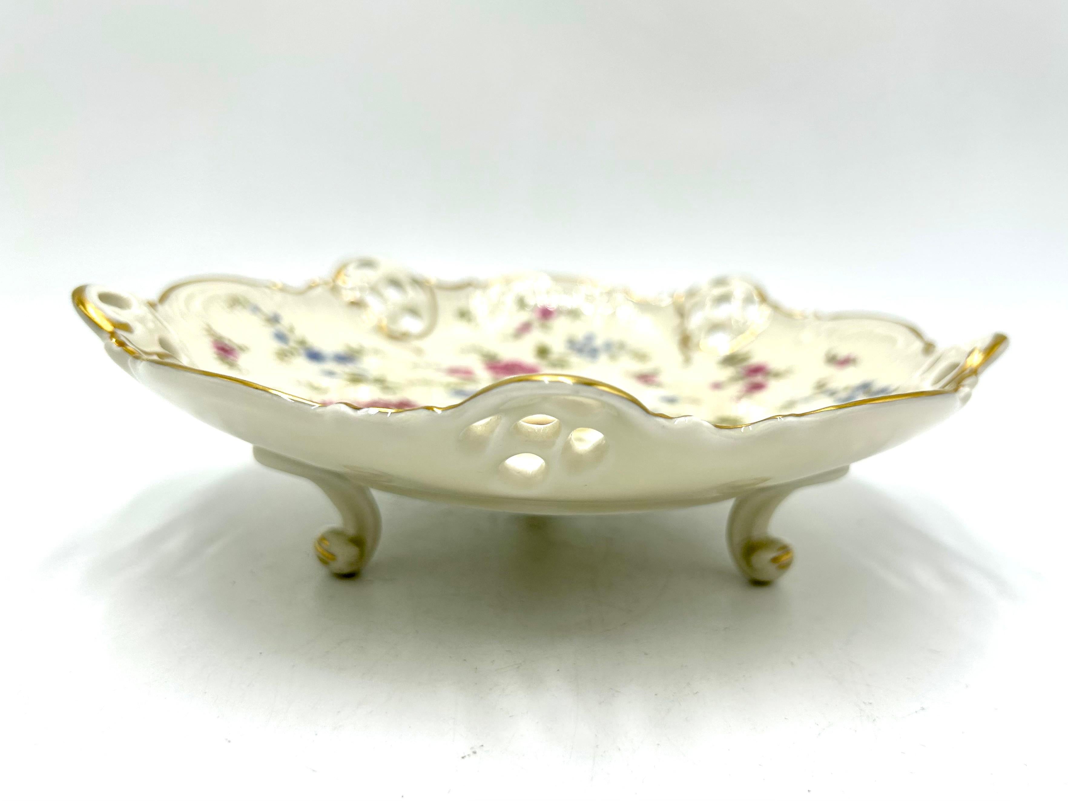 Openwork plate supported on three filigree legs from the Moliere collection, the renowned German Rosenthal label. The product is marked with the mark used in 1945. Ecru porcelain decorated with openwork sides, floral meadow motif and gilded