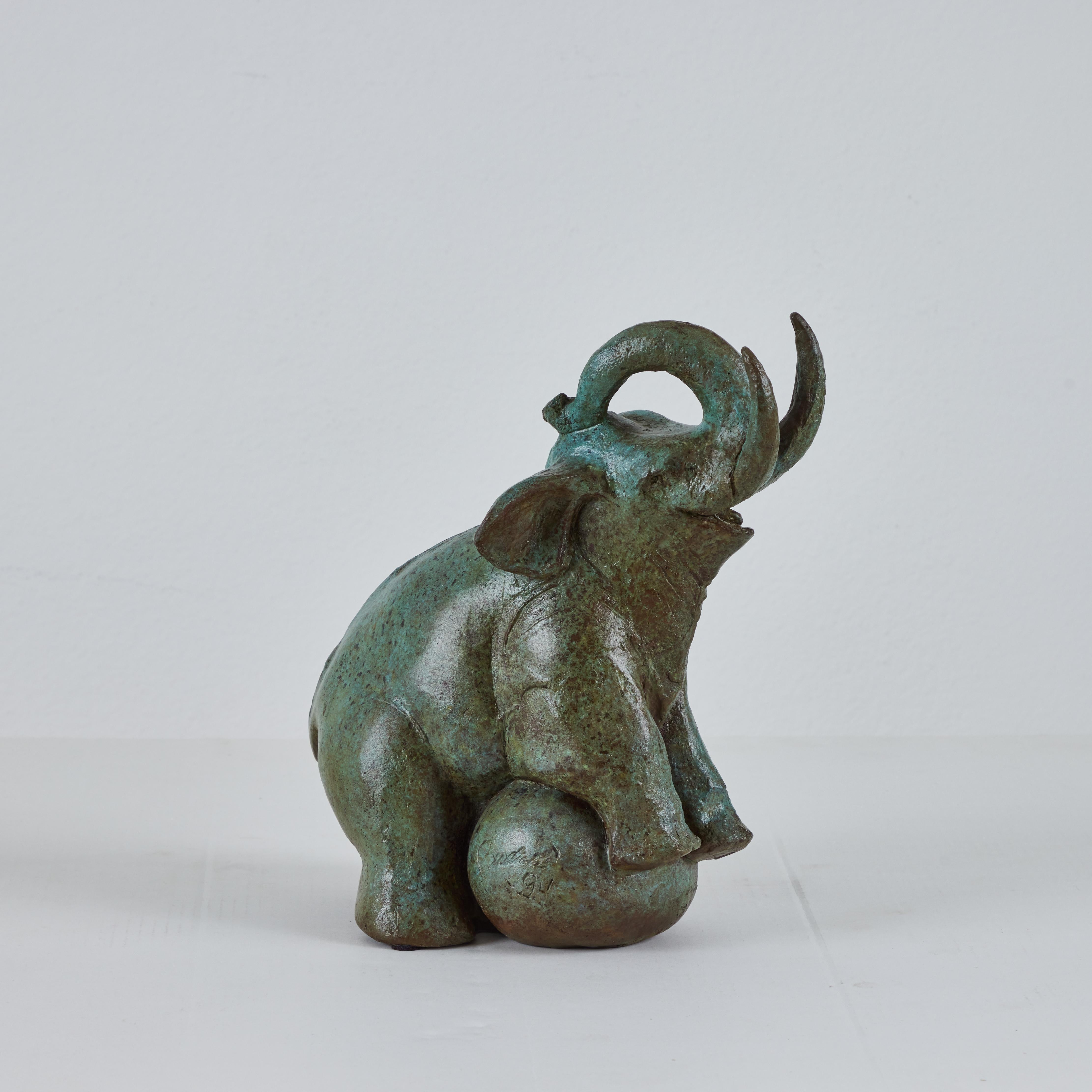 This is a beautifully sculpted bronze elephant by Barbara Beretich. The elephant comes across as a playful with one of his front legs raised on a ball much like a circus elephant. His trunk is curled up and tusks raised.  the bronze is signed on the