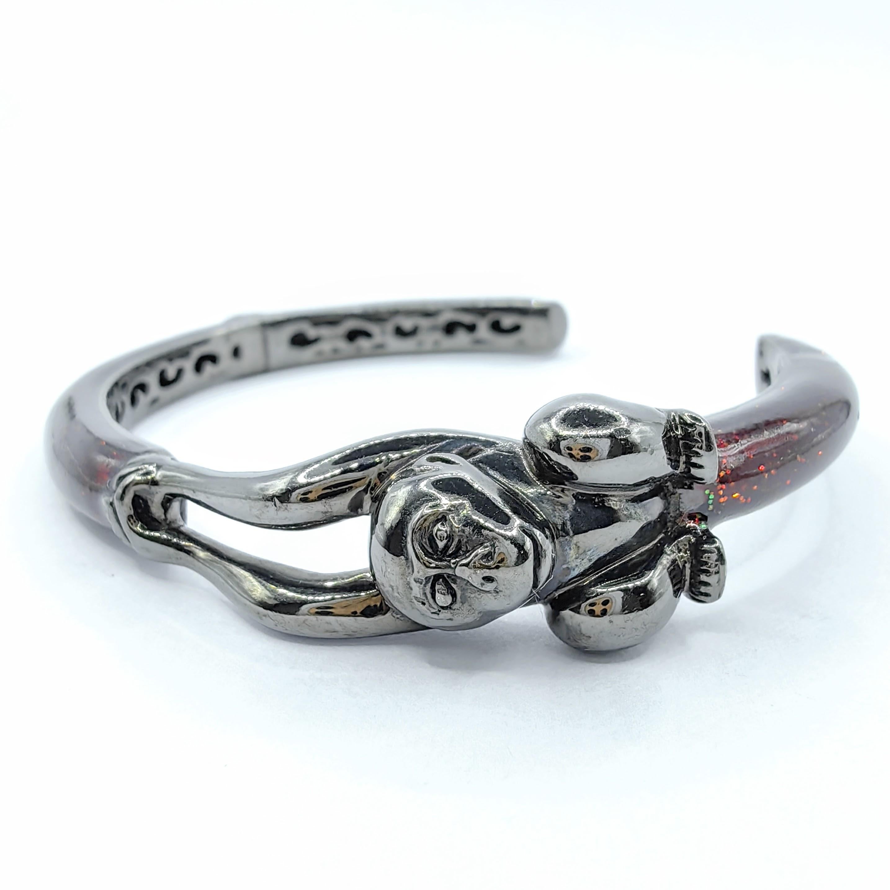 Verleihen Sie Ihrer Schmucksammlung einen Hauch von Skurrilität und Raffinesse mit dem Playful Monkey on Glittered Dark Red Emaille Cuff Bracelet in Sterling Silver. Dieses entzückende Armband zeigt eine charmante Affenfigur, die anmutig auf der