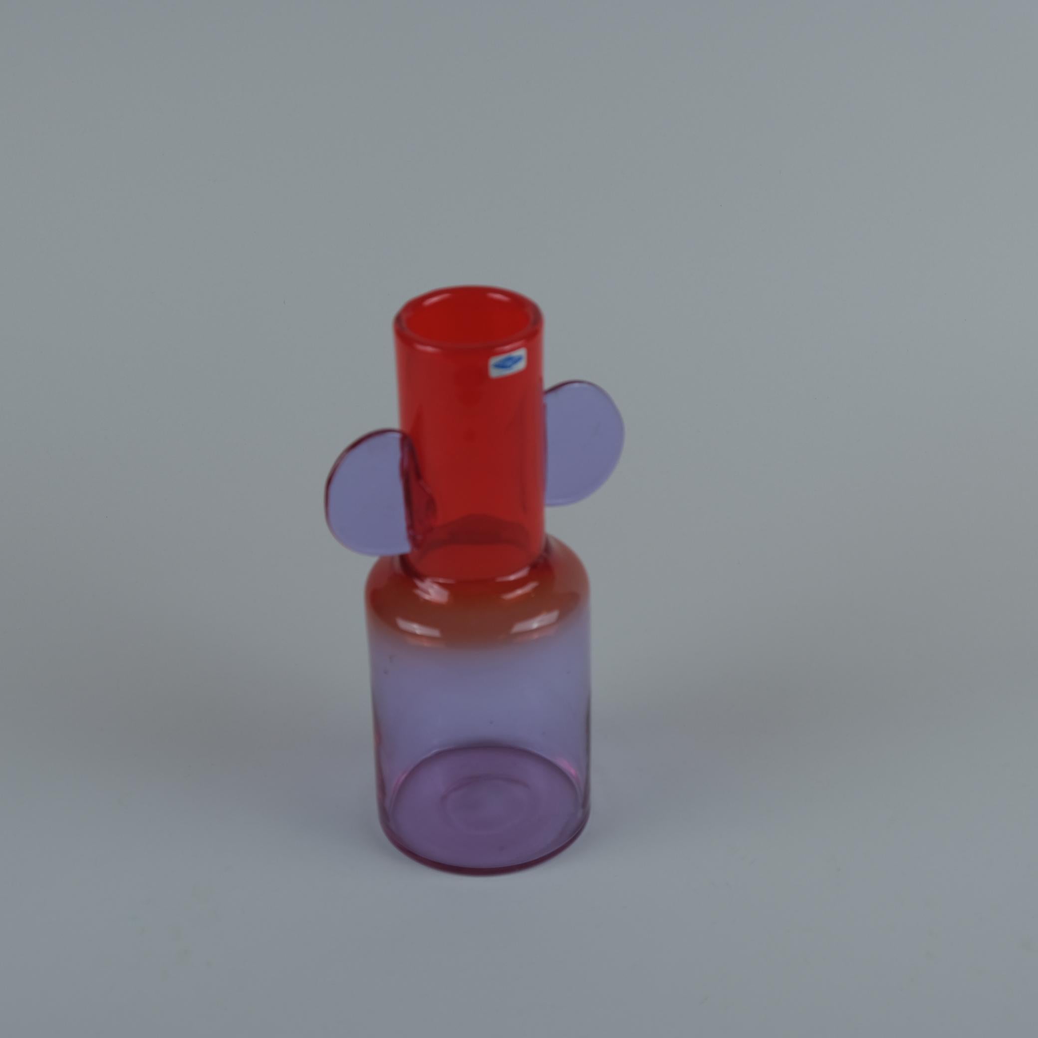Un vase spectaculaire et charmant en verre lavande et rouge soufflé dans un moule avec des décorations ajoutées sur les côtés. Conçu par le célèbre designer Oiva Toikka, connu pour ses dessins colorés et singuliers, ce vase porte la marque de