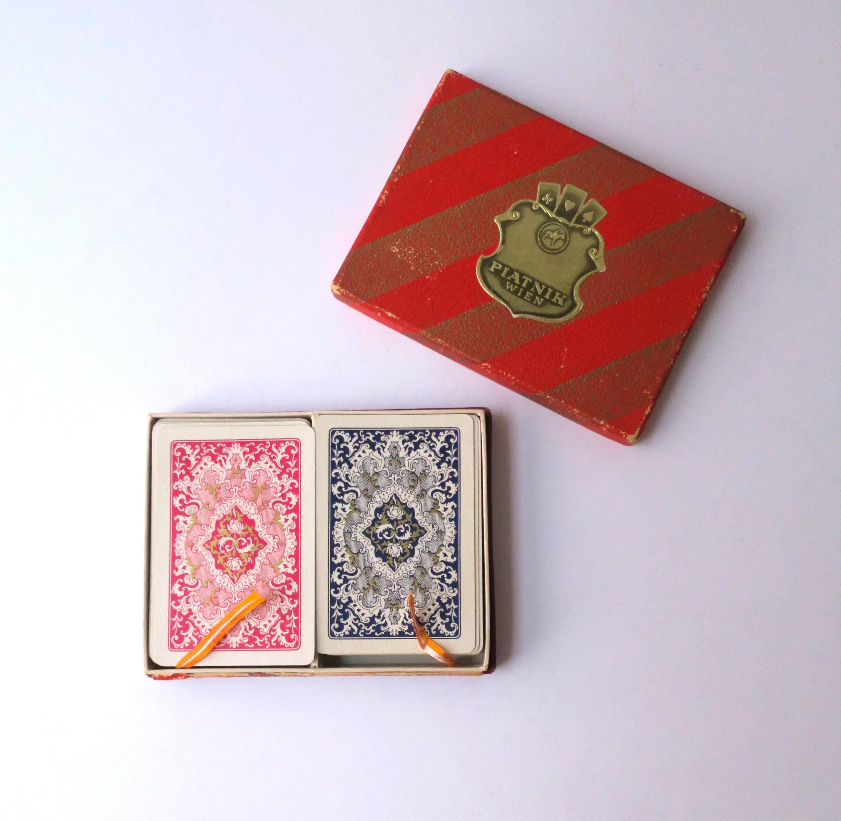Two (2) complete playing card decks with original red box, circa ealry-20th century, Austria. Set includes two complete playing card decks in box with silk pulls for easy removal of cards. Box dimensions: 4.07