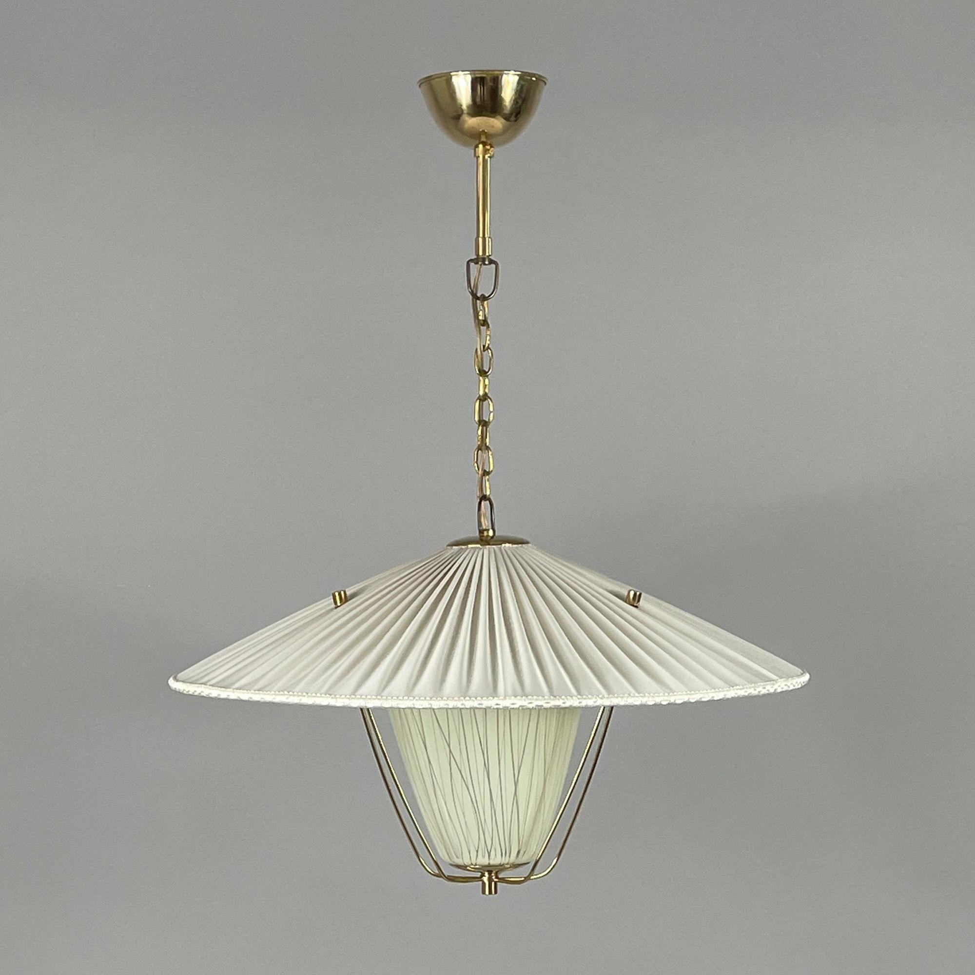 This elegant mid-century pendant was designed and manufactured in Austria in the 1950s.

The light features a pleated cream colored fabric shade, reminiscent of a wide-brimmed parasol, which is a common design motif from that era. 

The central pale