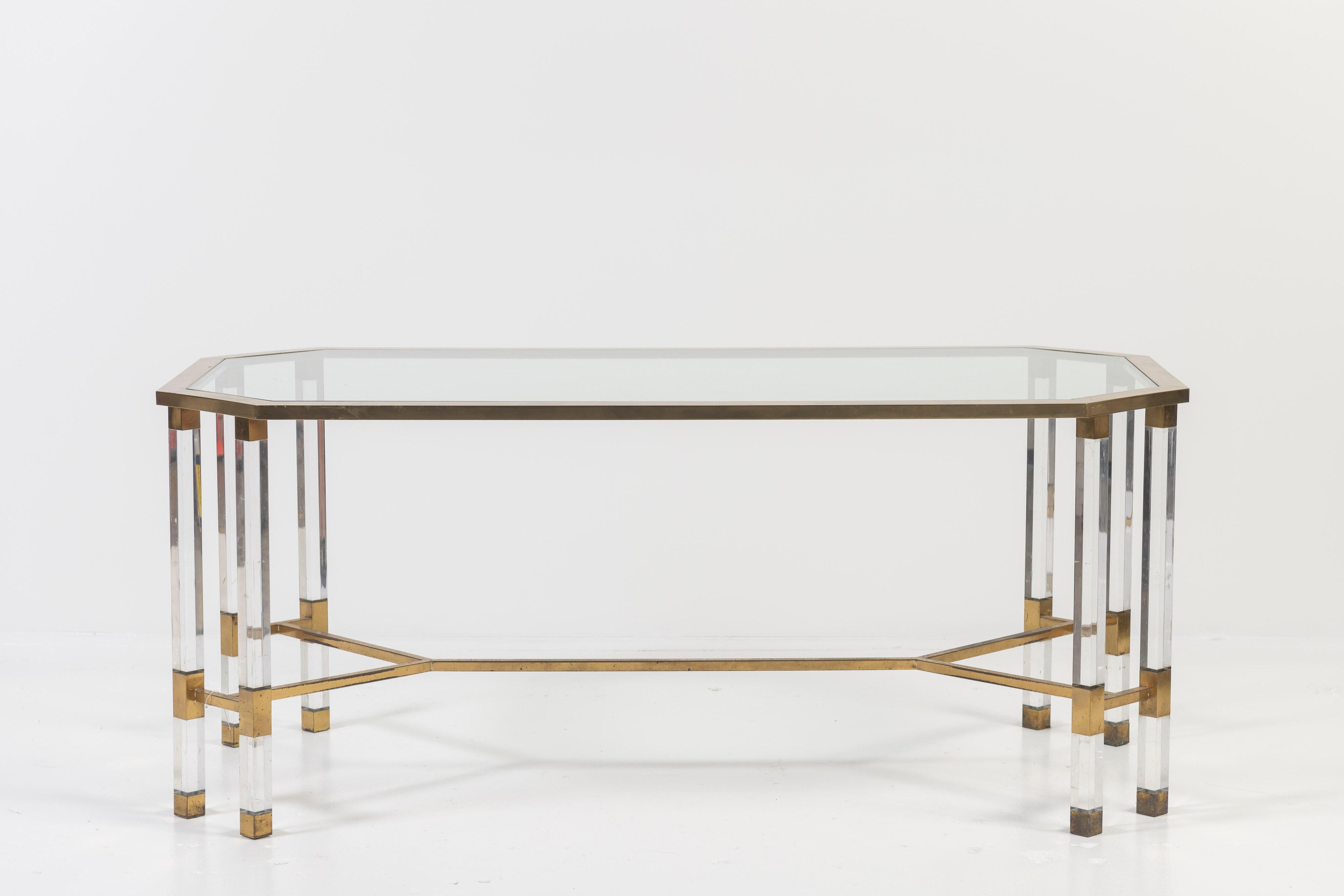 This 1970's plexiglass, glass and brass coffee table in the style of Charles Hollis Jones has a hexagonal shape with 8 legs, 4 on each corner, and an 