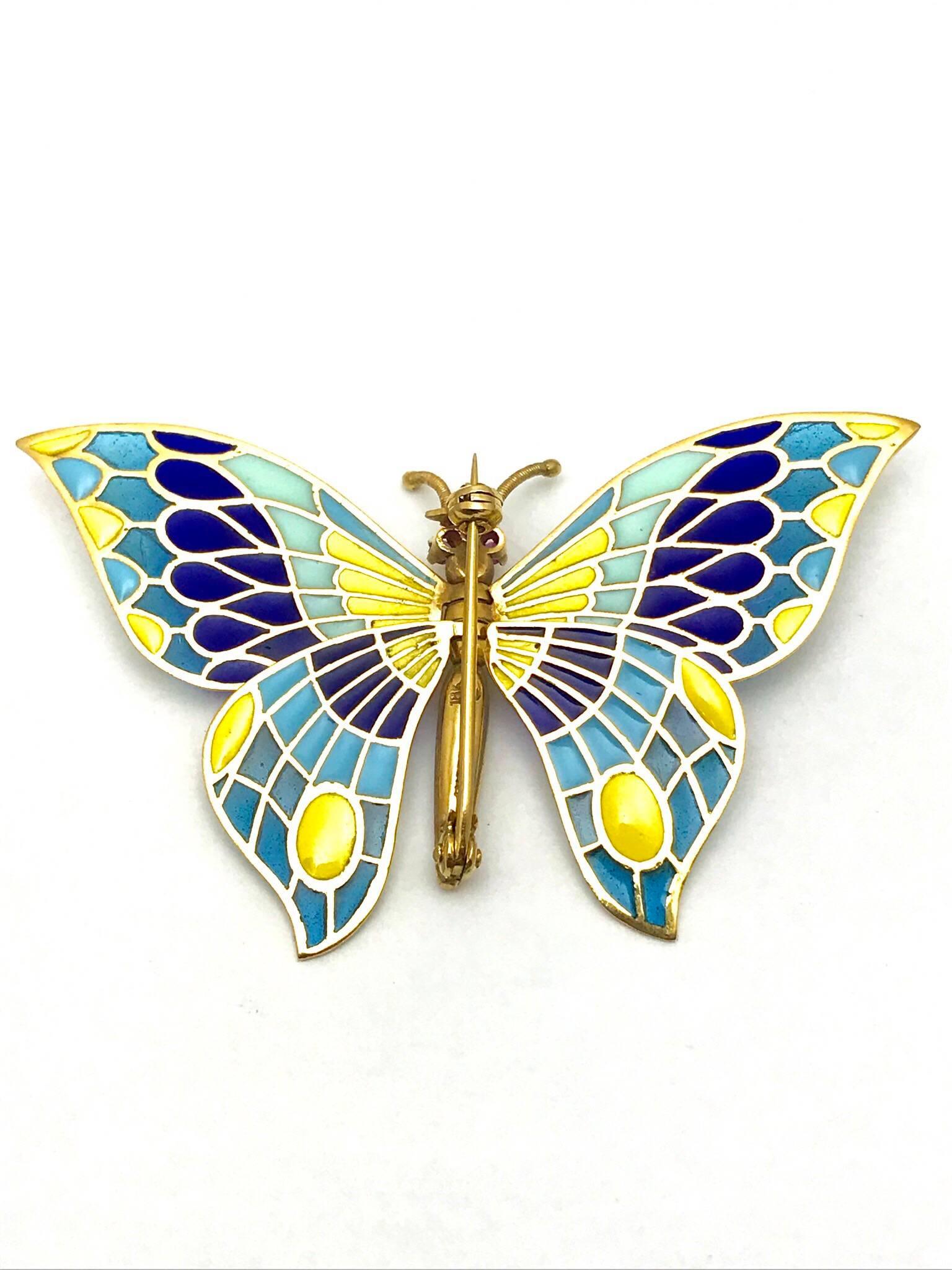 A plique a jour enamel and ruby eye 18 karat yellow gold butterfly brooch with articulating wings.  The butterfly features a textured gold body, with wings of  light blue, dark blue, and yellow colors.  The wings are able to fold all the way up, and