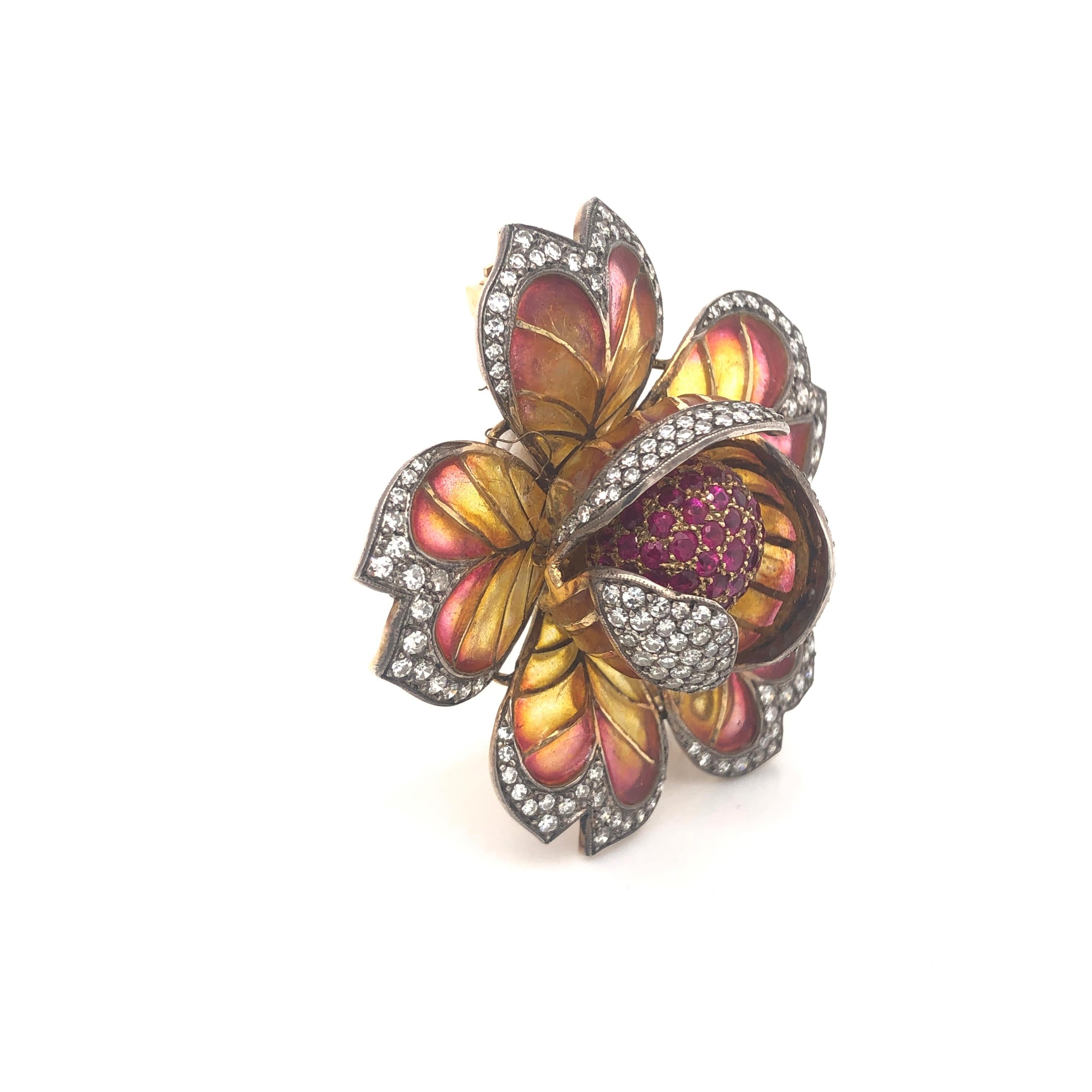 A Moira design orange to yellow plique-a-jour enamel flower brooch, with a pavé set ruby centre, and diamonds set to the outer petal edges, with a millegrain edge. Mounted in gold, with a pin and roller catch fitting. Signed Moira and numbered 5239.