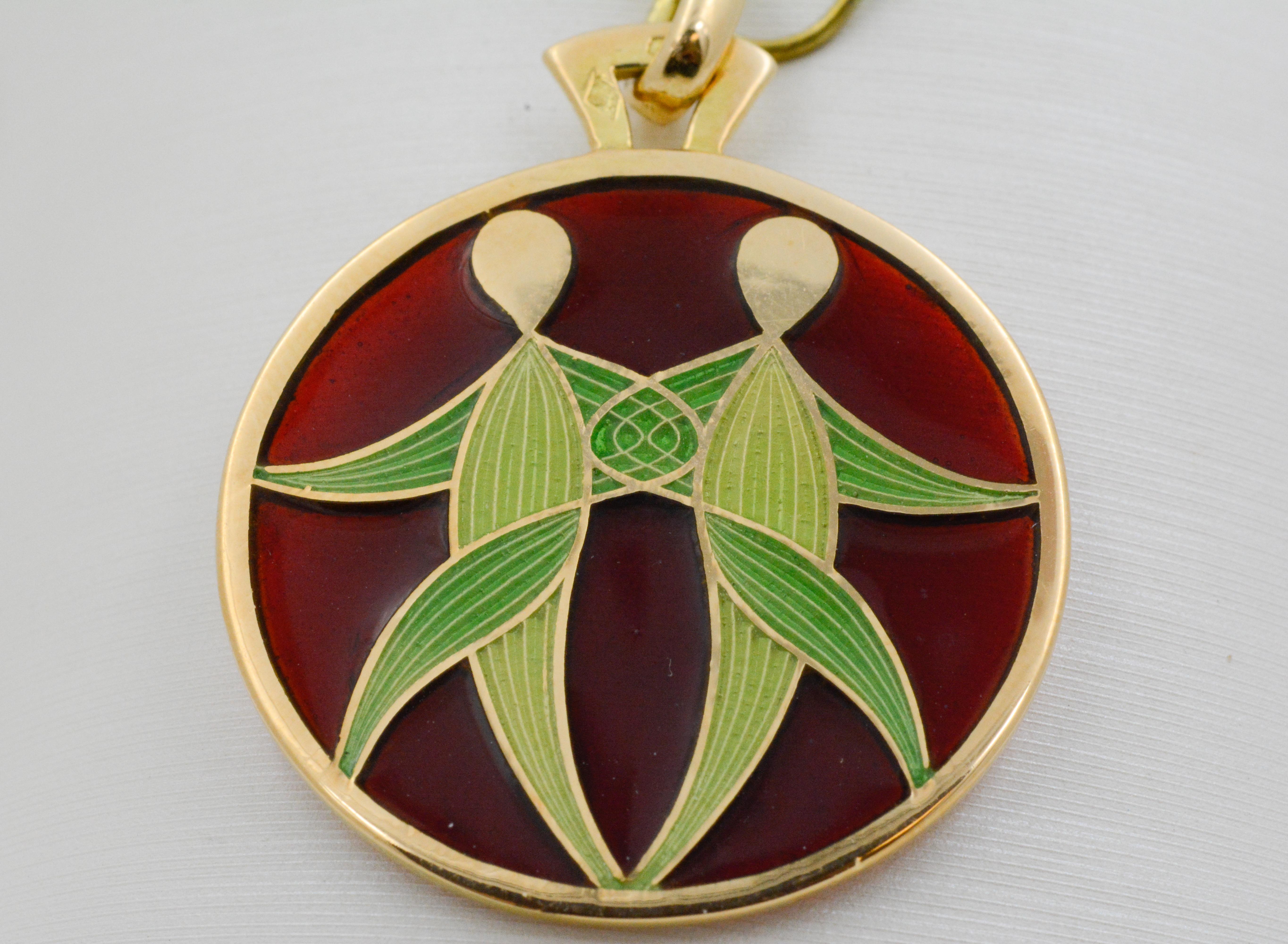 On a background of brownish red, the pale green glass Gemini zodiac sign has been expertly crafted in the art of Plique a Jour. This delicate and intricate hand enameled glass has 18 karat gold outlining every detail. 