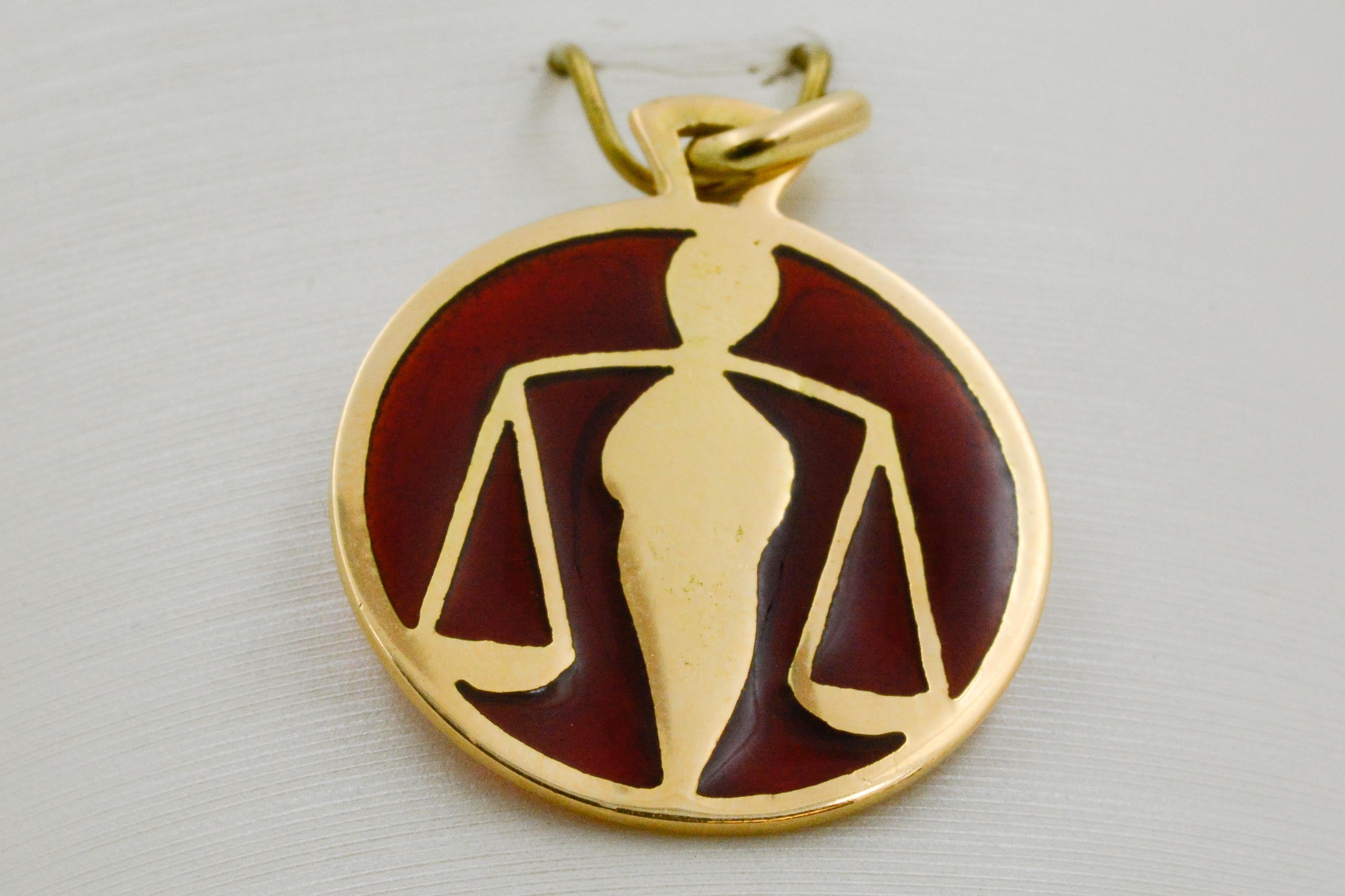 The Libra zodiac sign is showcased on this handcrafted enameled glass Plique a Jour pendant. The green and yellow Libra sign rests on an amber background with an 18 karat yellow gold outline. 

