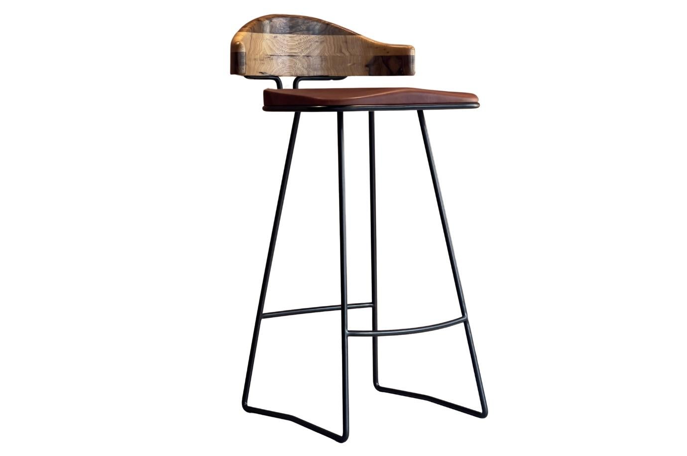 Plug Stool is a contemporary bar stool designed with both comfort and character in mind. It features an ergonomically shaped solid wood seat upholstered in cognac-tanned leather, paired with a gently curved solid wood backrest that provides support