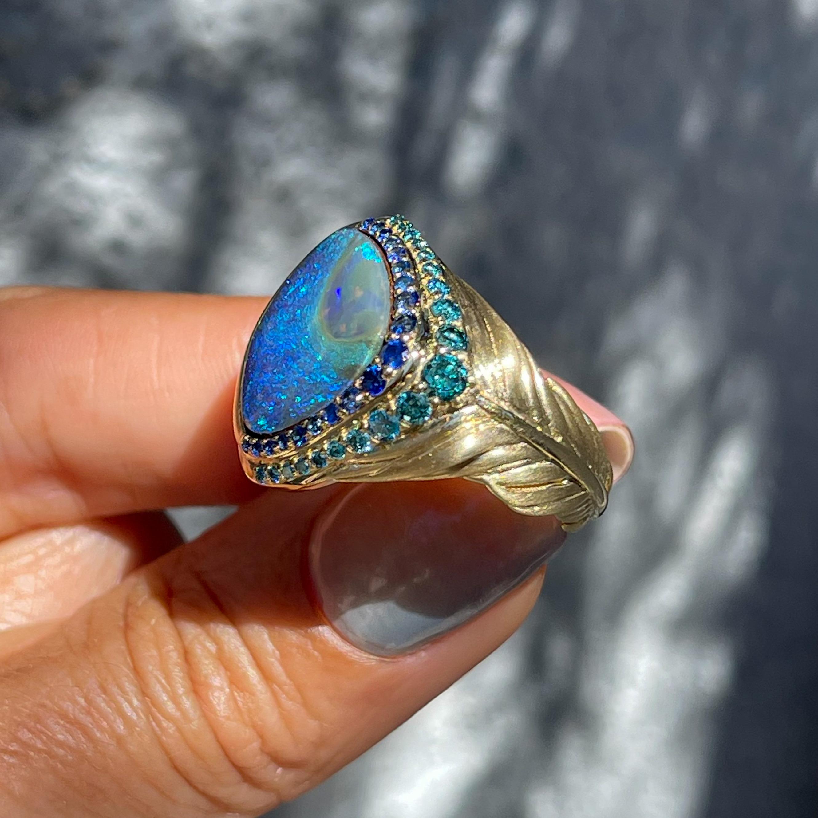 A striking boulder opal in peacock hues flashes from this Australian Opal Ring. Set in 14k gold with sapphires and diamonds, its display of colors is phenomenal. From the eyespot of the blue opal plume, shimmering cobalt swirls around an abyss of