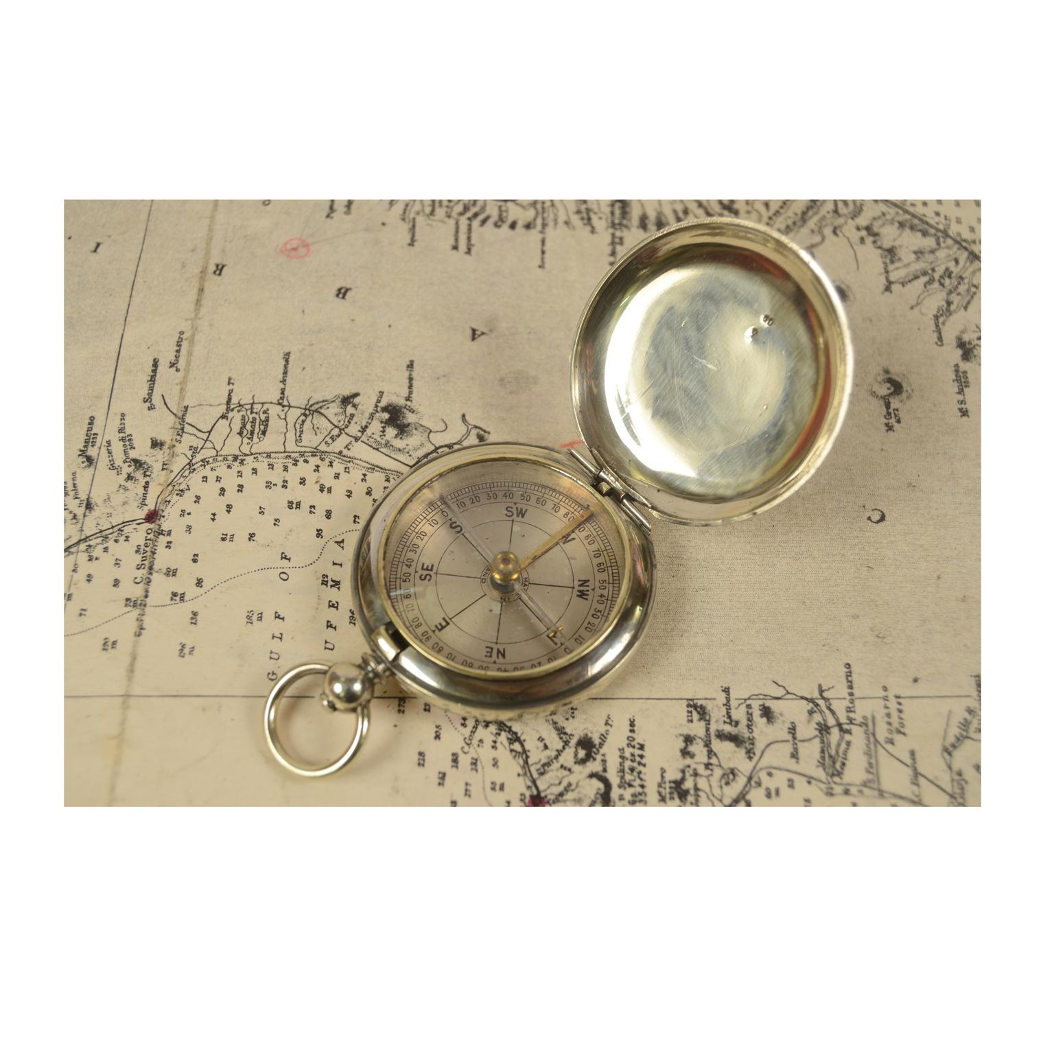 Officer's pocket compass of chromed brass in the shape of a pocket watch. English manufacture from the early 1900s. The compass is equipped with a lid with snap closure with release button inside the ring. Six-wind compass card complete with