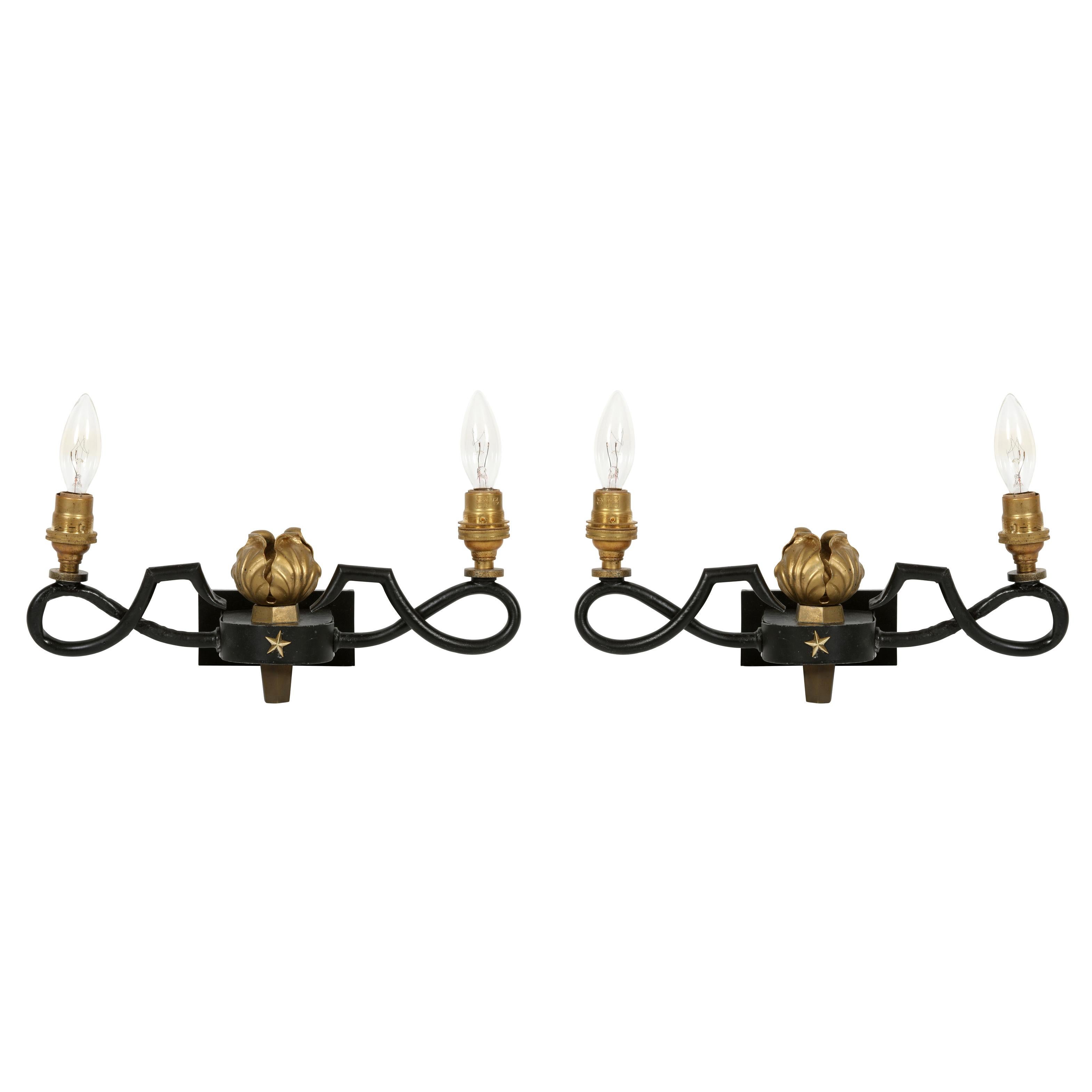 A pair of Gilbert Poillerat style black painted brass double arm wall sconces with acanthus and star gilt detail.