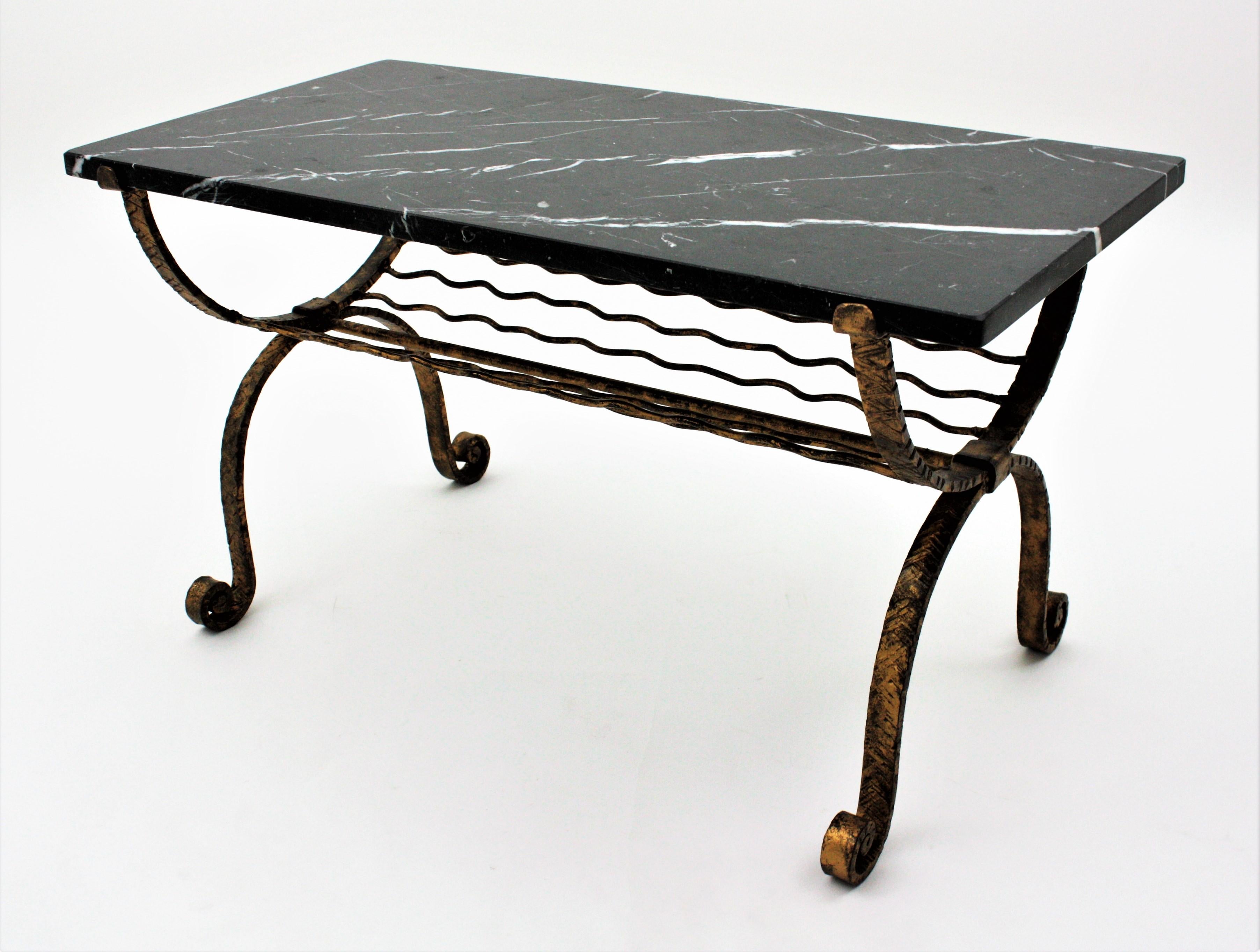 Wrought iron parcel-gilt coffee table with rectangular black marble top and magazine rack. France, 1940s.
Inspired in Gilbert Poillerat designs.
This beautiful table has a black Marquina marble top with white streaks. It stands up on a four iron