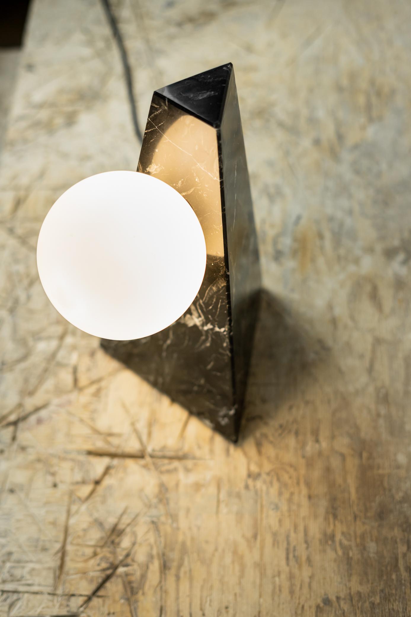 The concept of gravity and the interaction between two cosmic forms explored in a table lamp. Shown in polished black Marquina marble. Designed by Samuel Dos Santos for Essenzia.