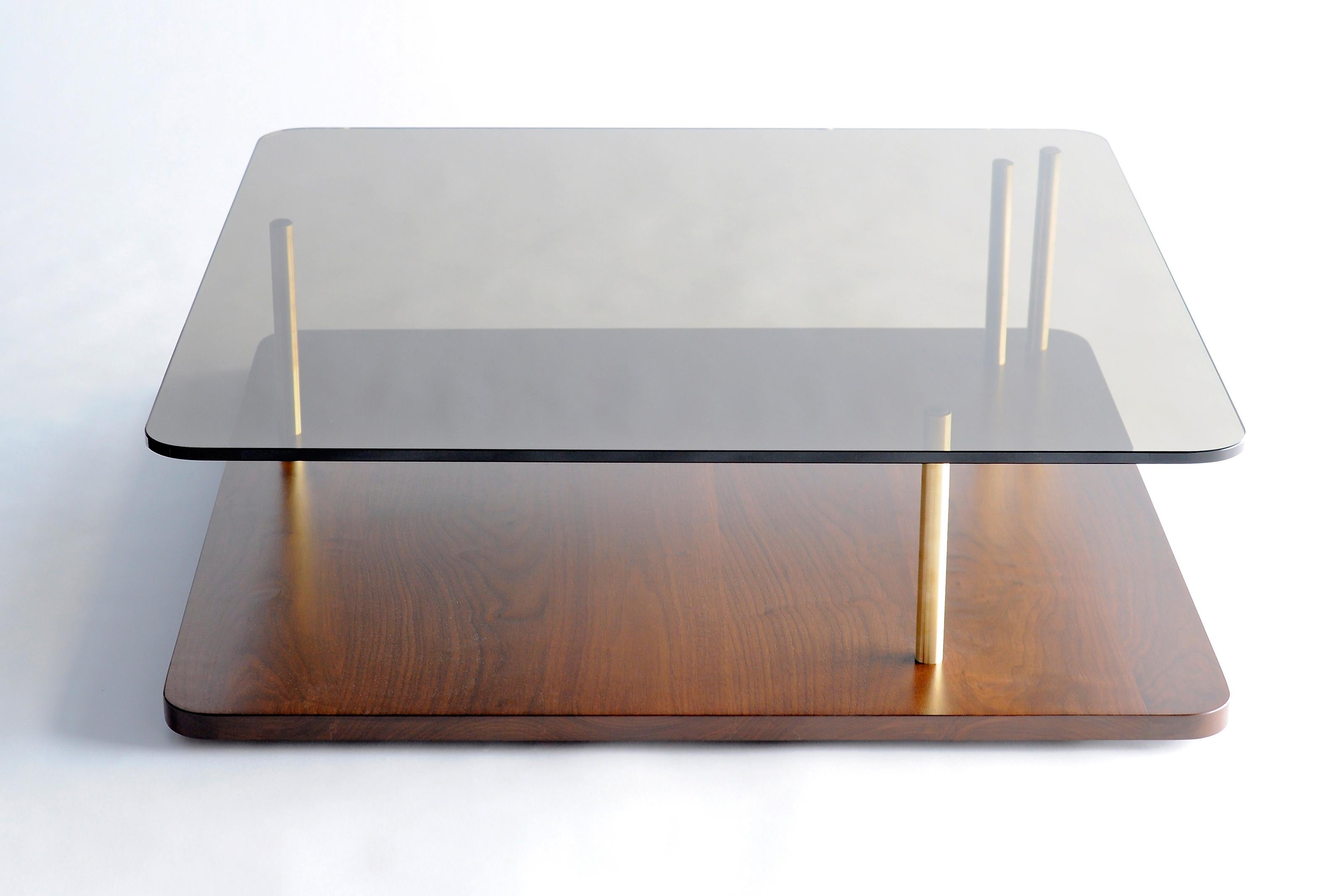 Points of Interest Square Coffee Table by Phase Design
Dimensions: D 96.5 x W 96.5 x H 29.2 cm. 
Materials: Walnut, glass and brass.

Solid wooden base is available in walnut, white oak, and ebonized oak. Support columns are available in solid