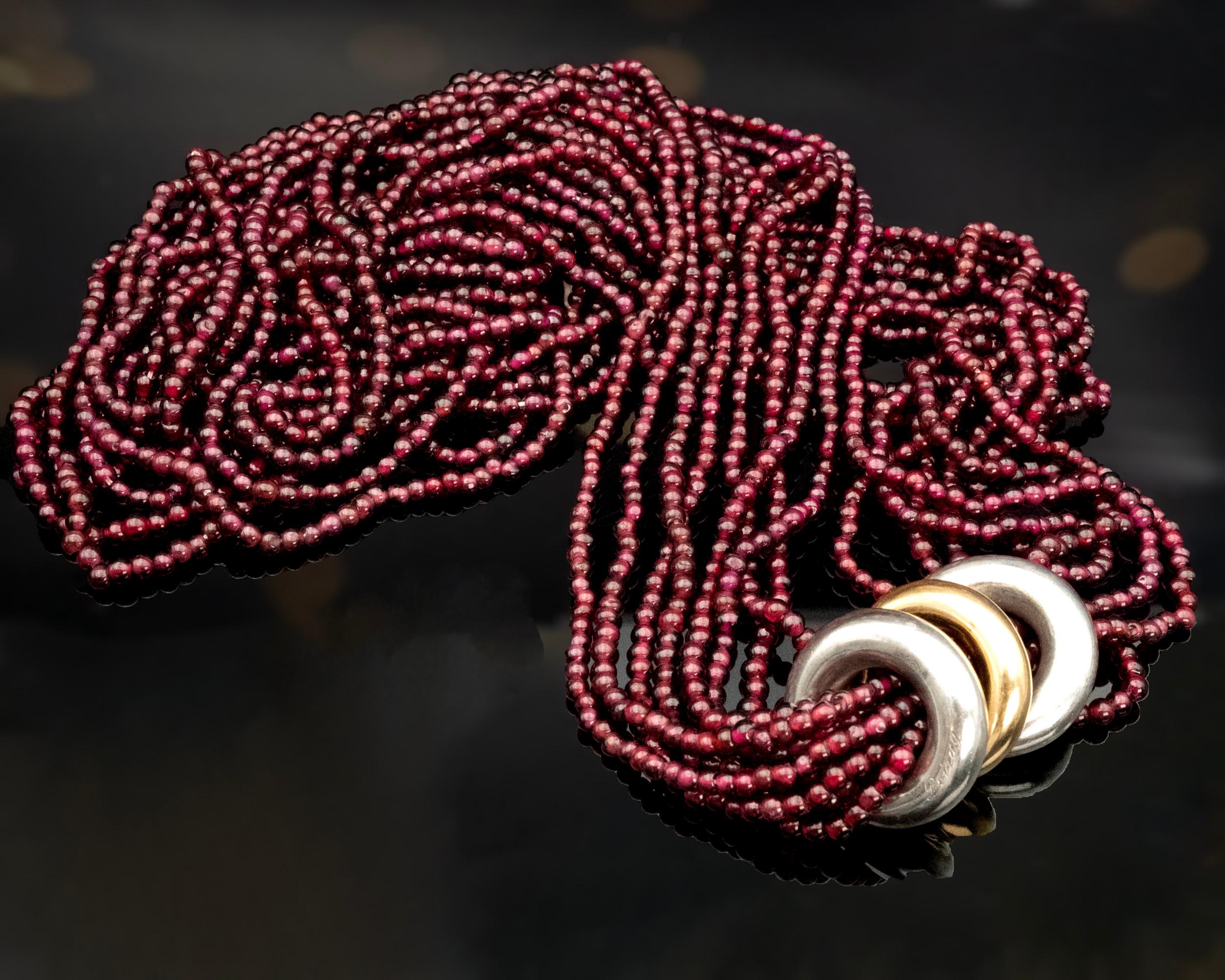 Auffällige mehrsträngige Sautoir-Halskette der renommierten Modemarke Poiray. Diese atemberaubende Halskette mit einer großzügigen Länge von 33 Zoll besteht aus acht Strängen mit leuchtenden Granatperlen. Drei kräftige Ringe in Form eines Doughnuts