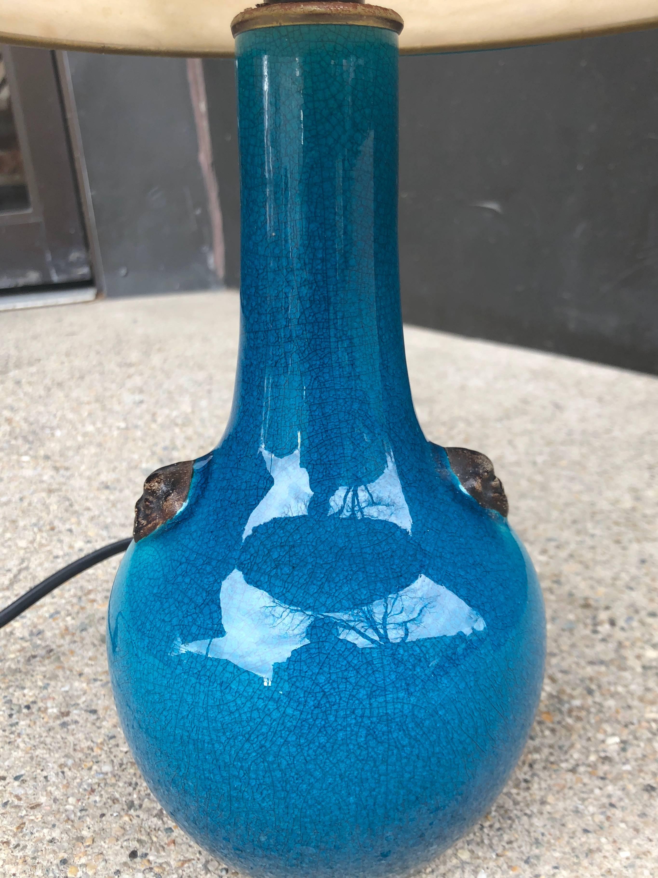 Lampe à glaçure craquelée bleu foncé avec un petit médaillon en forme de chien fu. L'abat-jour d'origine a une bordure bleue assortie. Le vase en céramique était à l'origine un pied de lampe. Signé en dessous 