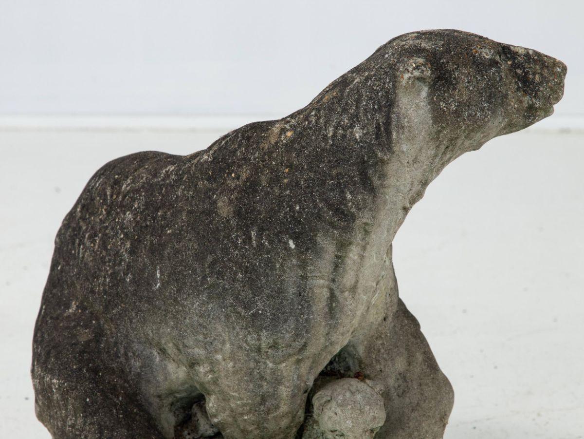 A cast stone garden ornament in the shape of a polar bear. The face and coat have lifelike detail. The front paw wraps around a Polar Bear cub also with wonderful detail. This concrete item is originally French from the early 20th century.