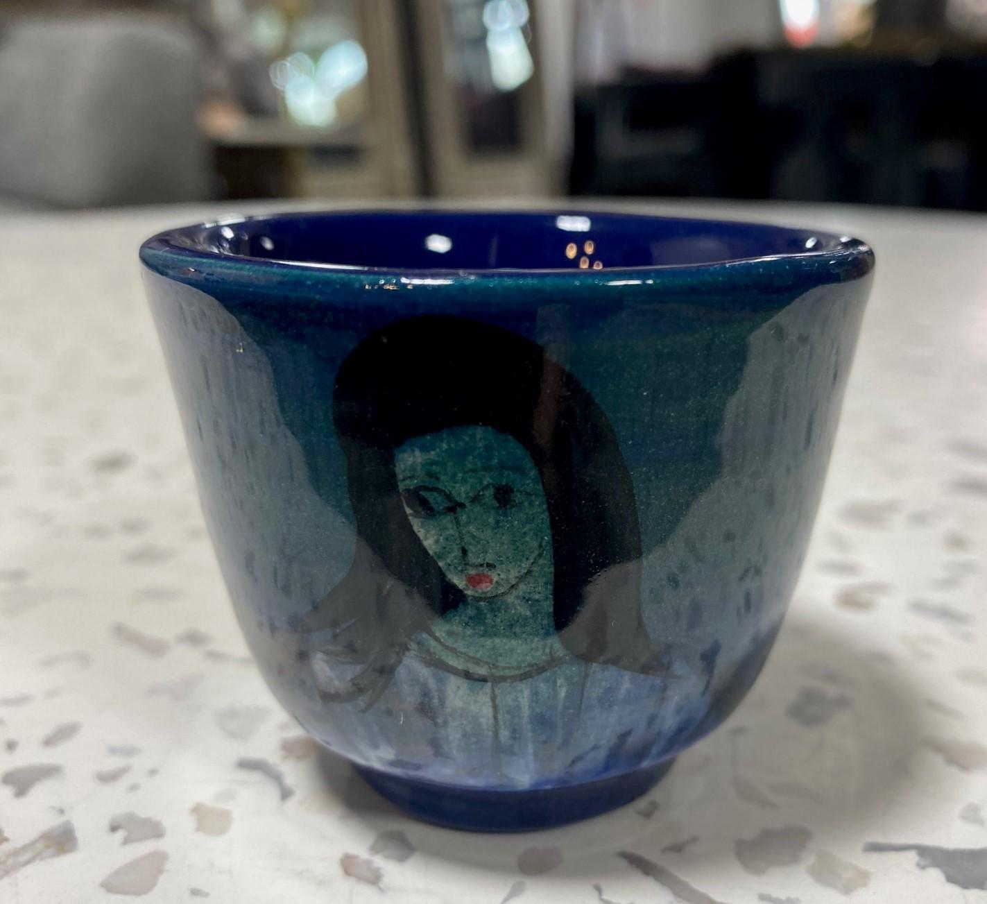 A wonderful, whimsical diminutive Yunomi tea cup by famed Polish-American master potter/artist Polia Pillin featuring a deep, rich cobalt blue glaze with streaks of green swirling around the cup body and hand painted female portrait figure.