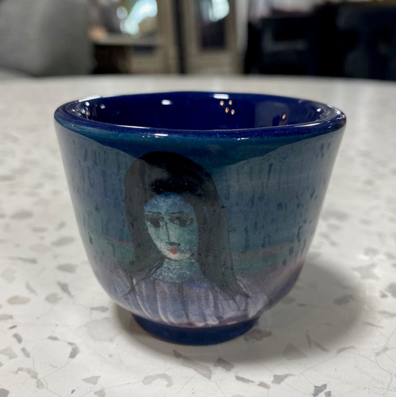 A wonderful, whimsical diminutive Yunomi tea cup by famed Polish-American master potter/artist Polia Pillin featuring a deep, rich cobalt blue glaze with streaks of green swirling around the cup body and hand painted female portrait figure.