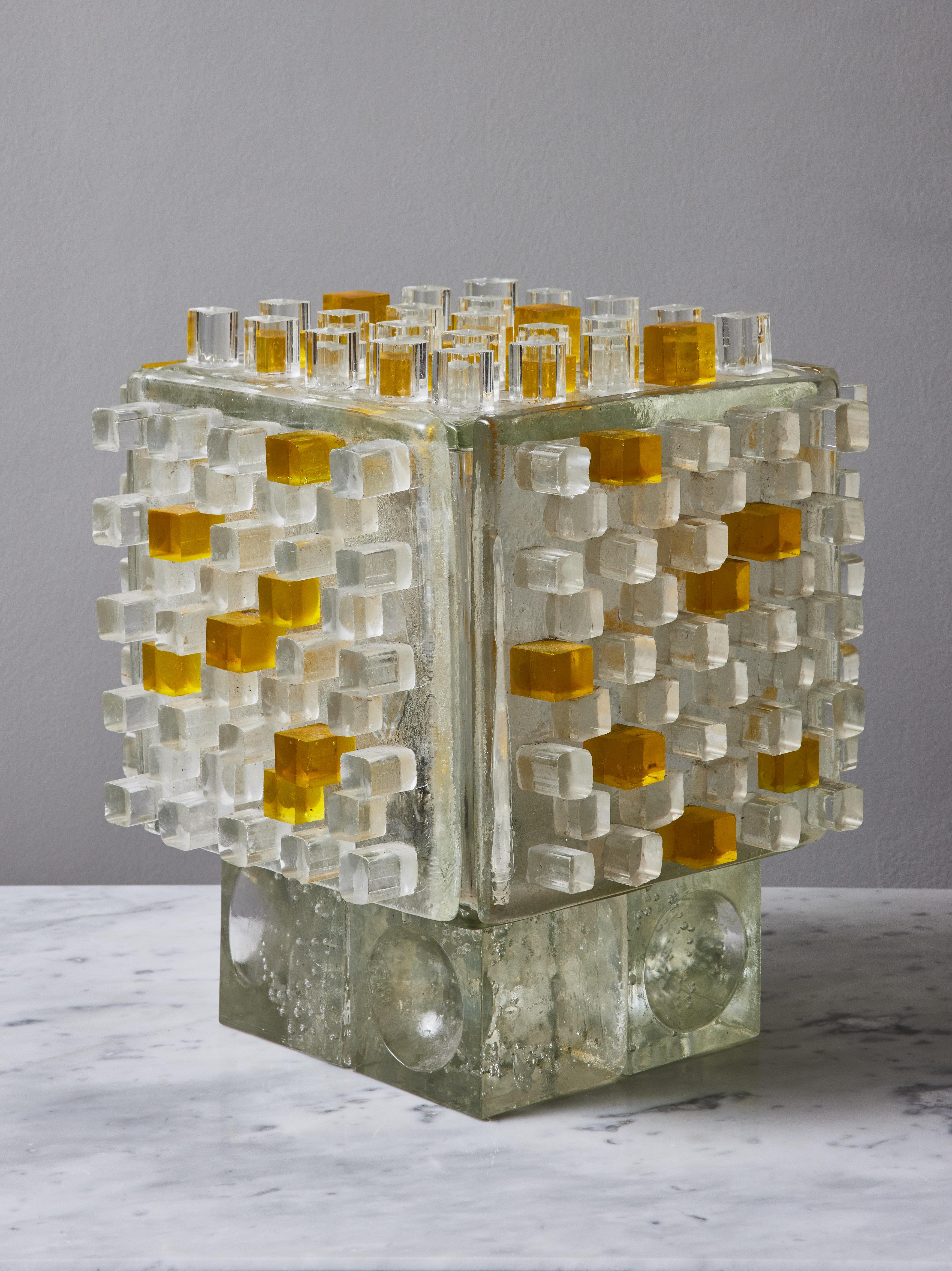 Surprising cube table lamp made of thick glass slabs on which are glued squares of clear and yellow lucite. One single light bulb inside.