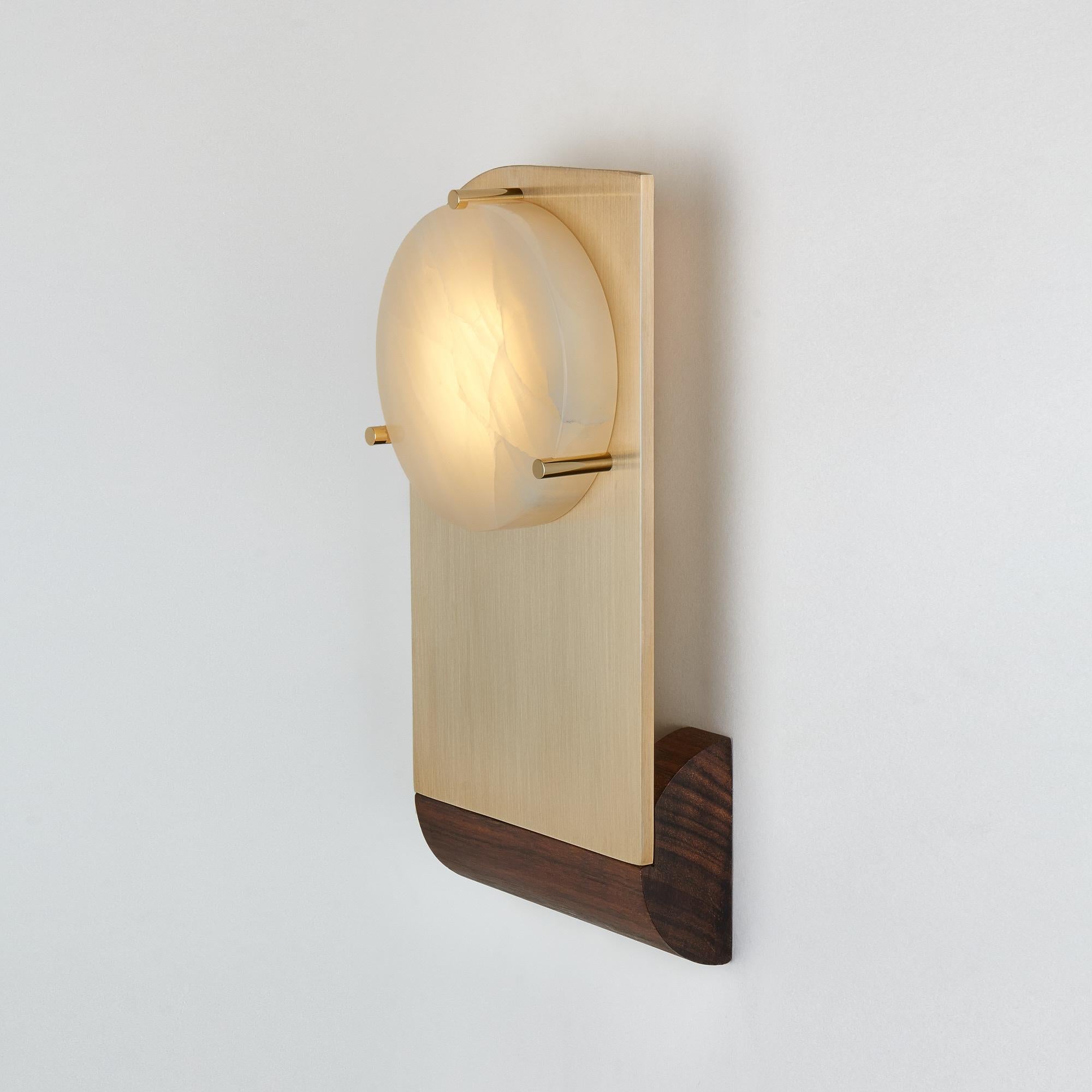 Polifemo sconce is a composition of three natural elements, alabaster, brass, and mongoy wood complementing each other through a dialogue of pure geometries.
The name of the piece refers to the Cyclope because of the giant eye glowing light from a