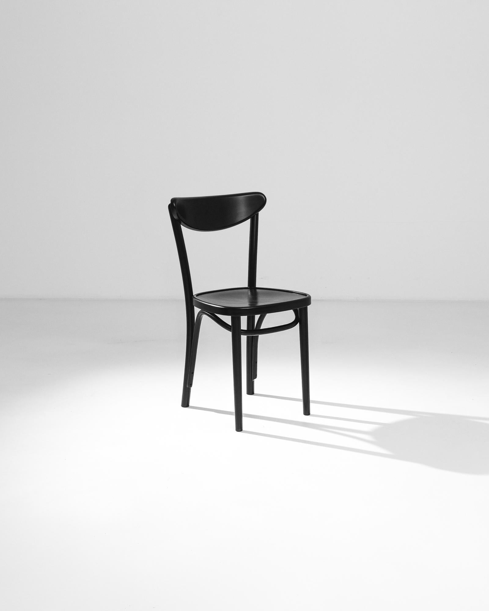 A wooden chair from Poland. The graceful lines of the bentwood legs recall the iconic designs of Thonet; a curved backrest and the gentle indentation of the seat create a sense of comfort and ease. The sleek, black-painted finish of the wood